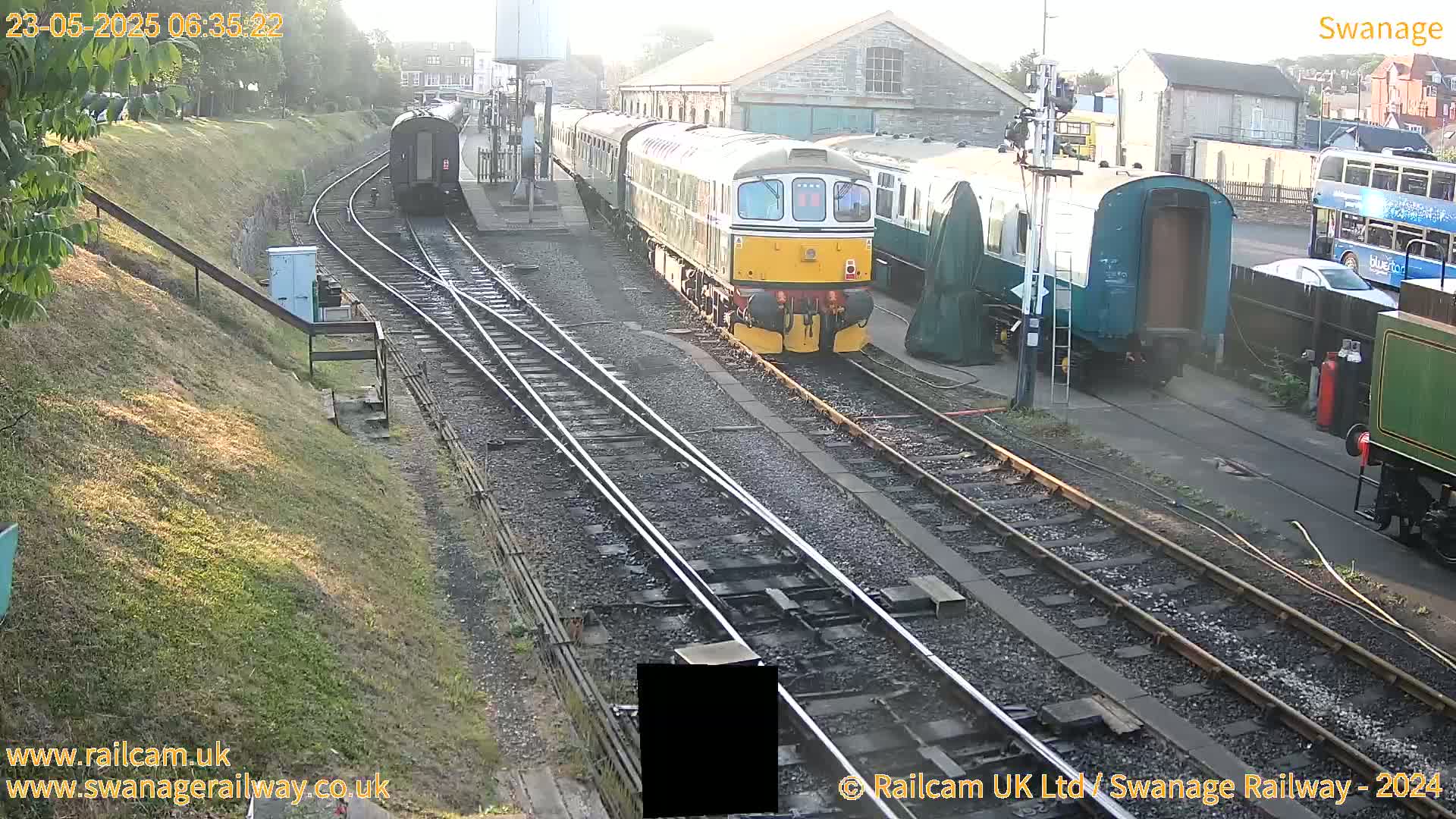A passenger train sits in a railway station on a sunny morning.