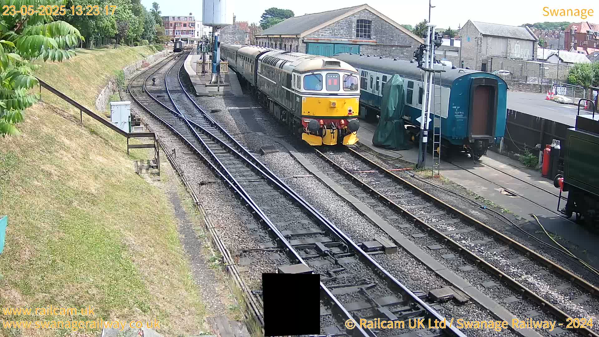 A yellow and brown diesel locomotive leads a train of passenger cars along a railway track on a sunny day.