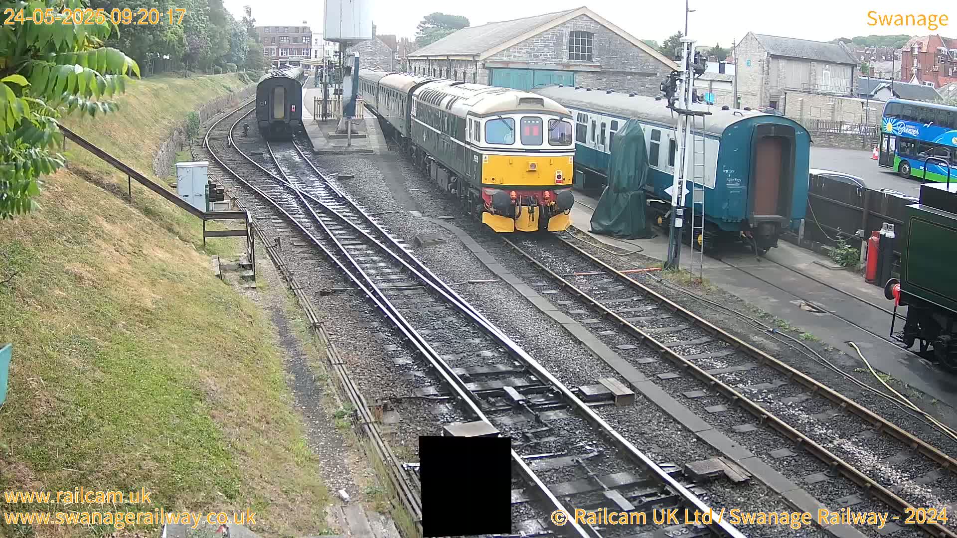A diesel locomotive leads a train of passenger cars at a railway station on an overcast day.