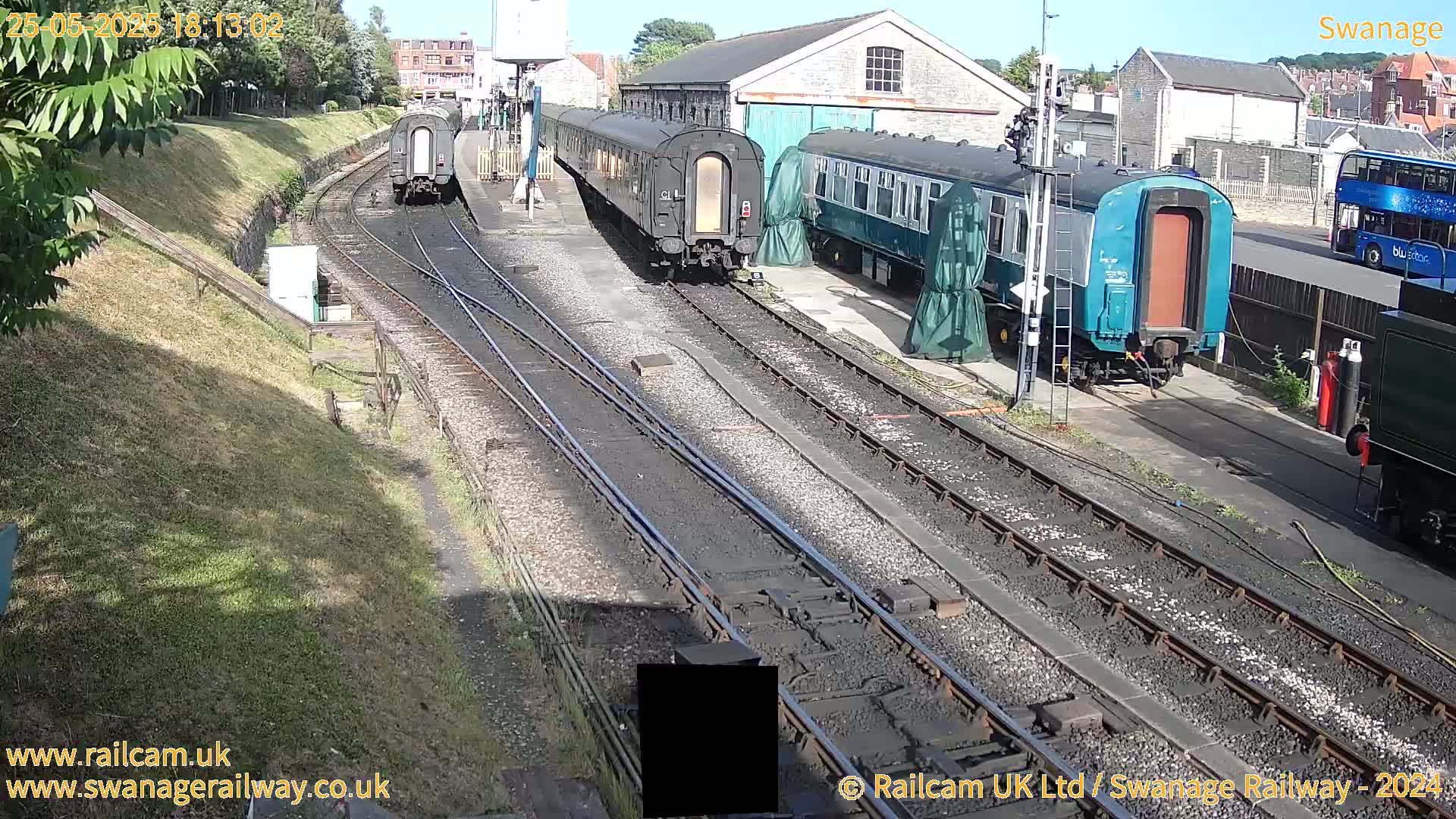 Several railway carriages are parked on train tracks beside a railway station on a sunny day.