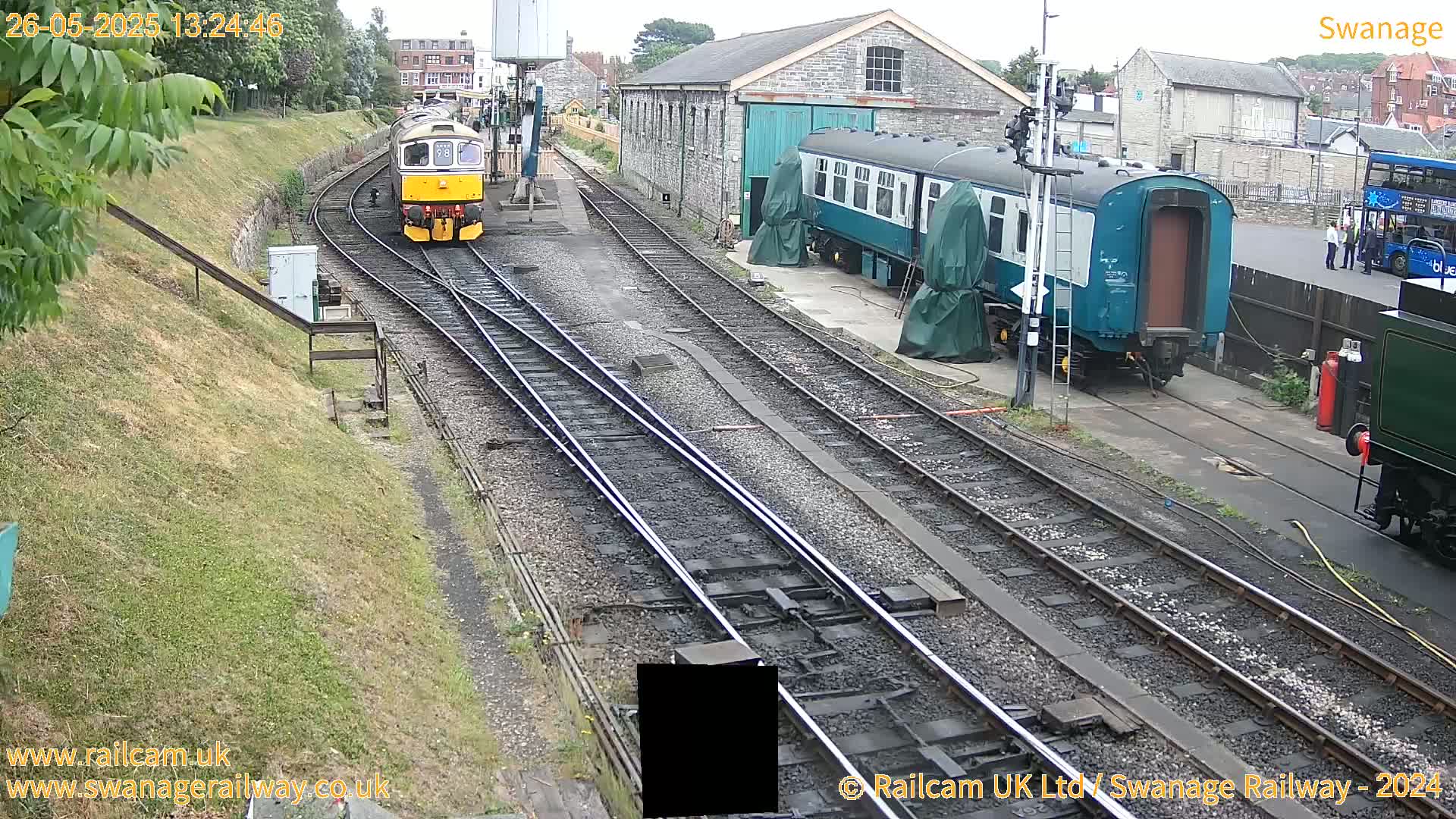 A railway yard with several train cars, including a diesel locomotive and passenger cars, on a partly sunny day.