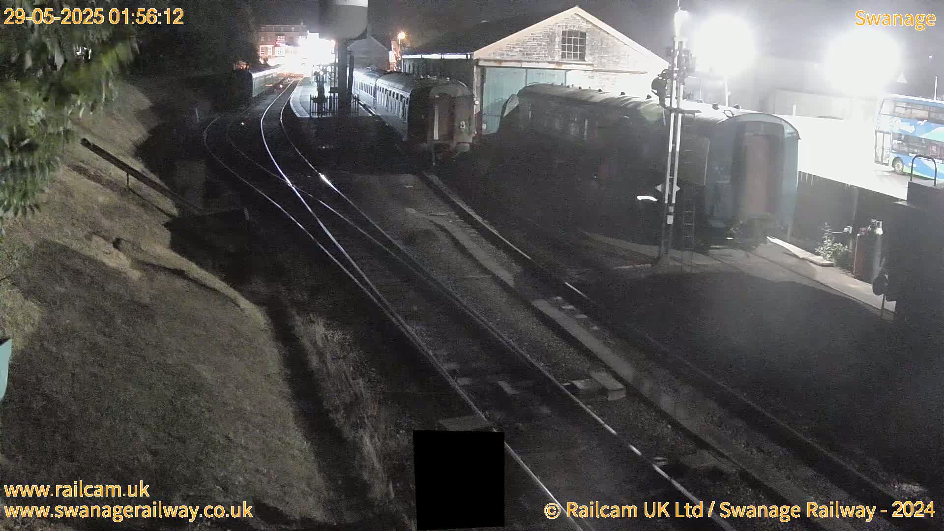 At night, railway cars sit on tracks next to a building, with a sloped embankment visible to the left.