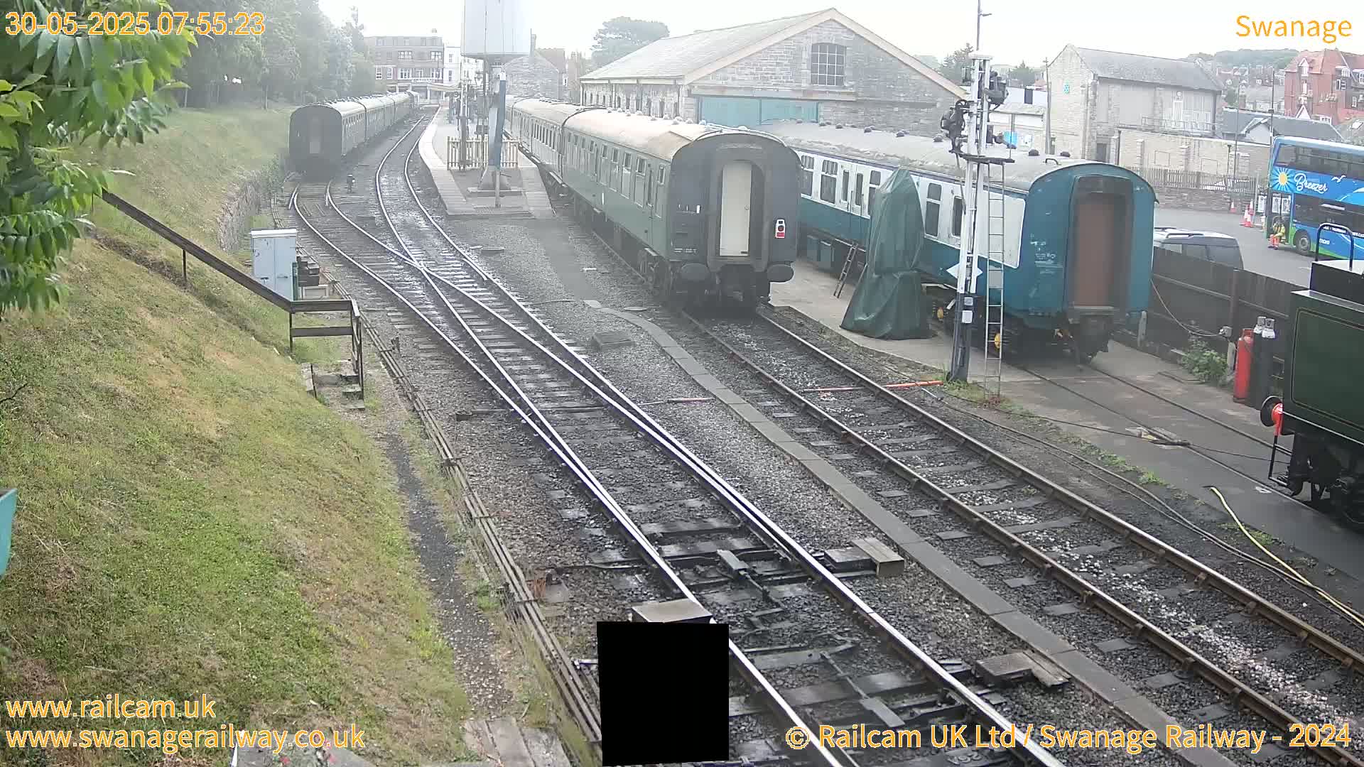 Several railway carriages are parked on a track beside a railway station on an overcast day.