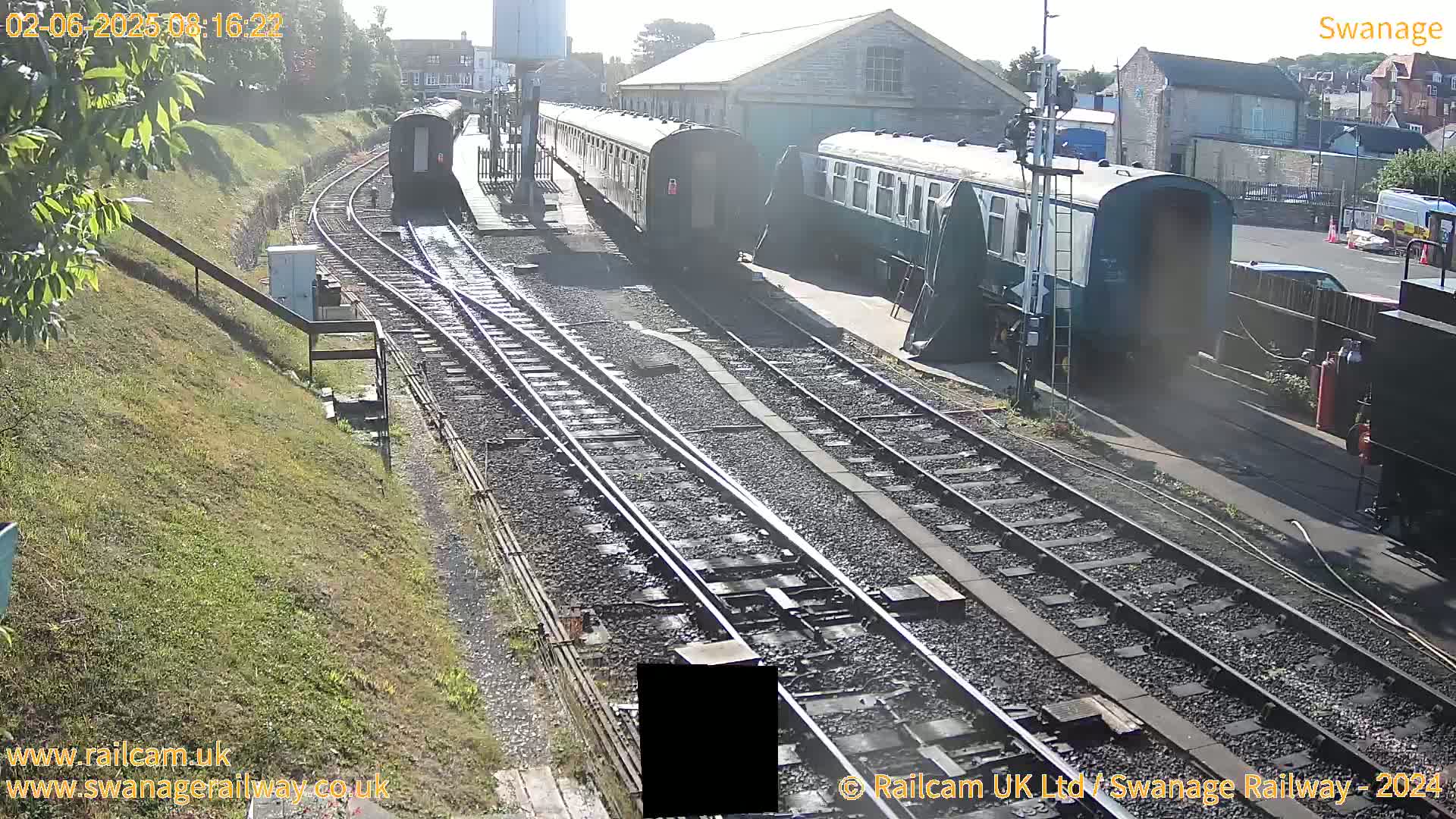 Several railway cars are parked on a sunny day next to train tracks in a railway yard.