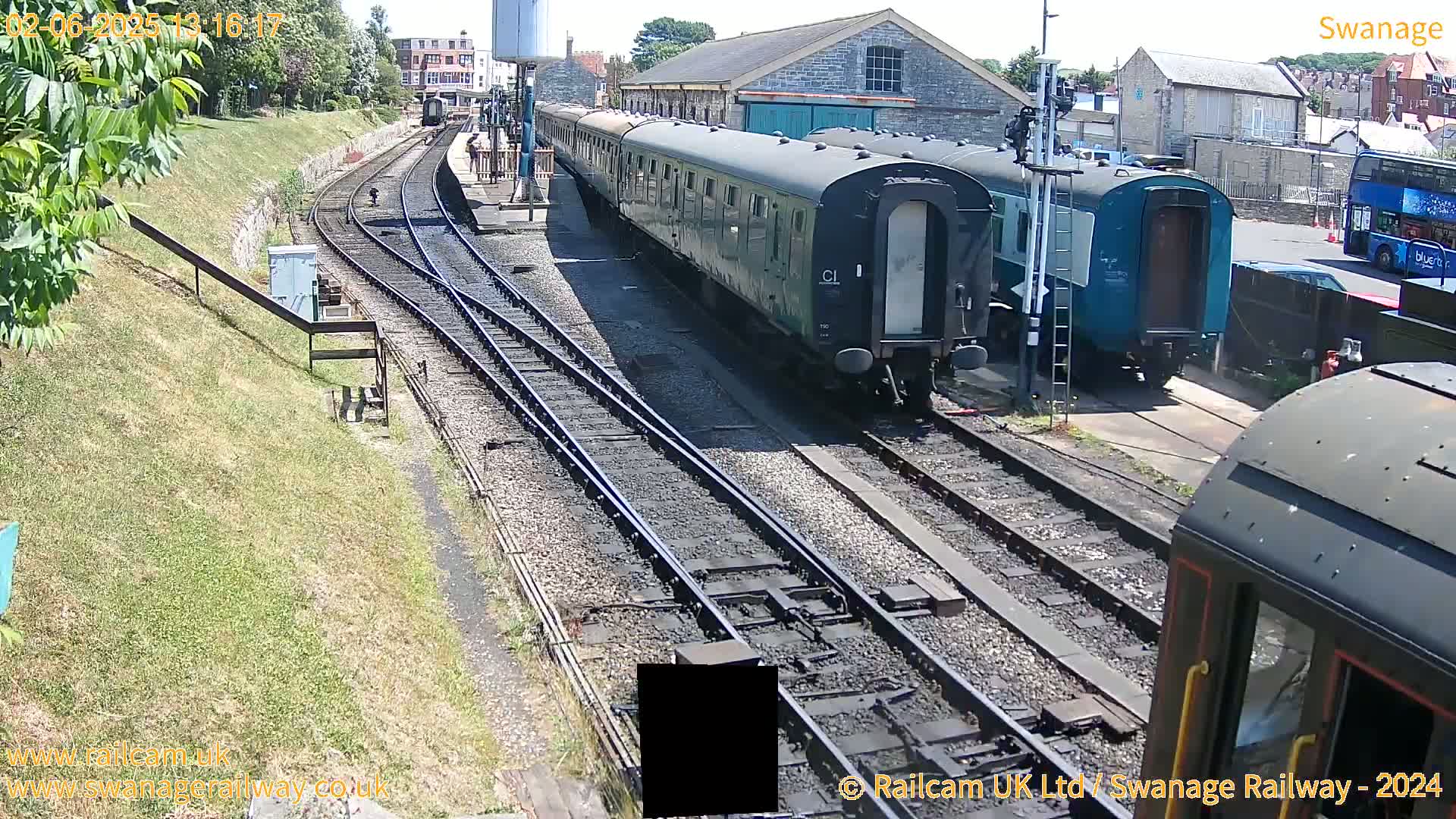 Several railway carriages are parked at a station on a sunny day; two sets of train tracks are visible.