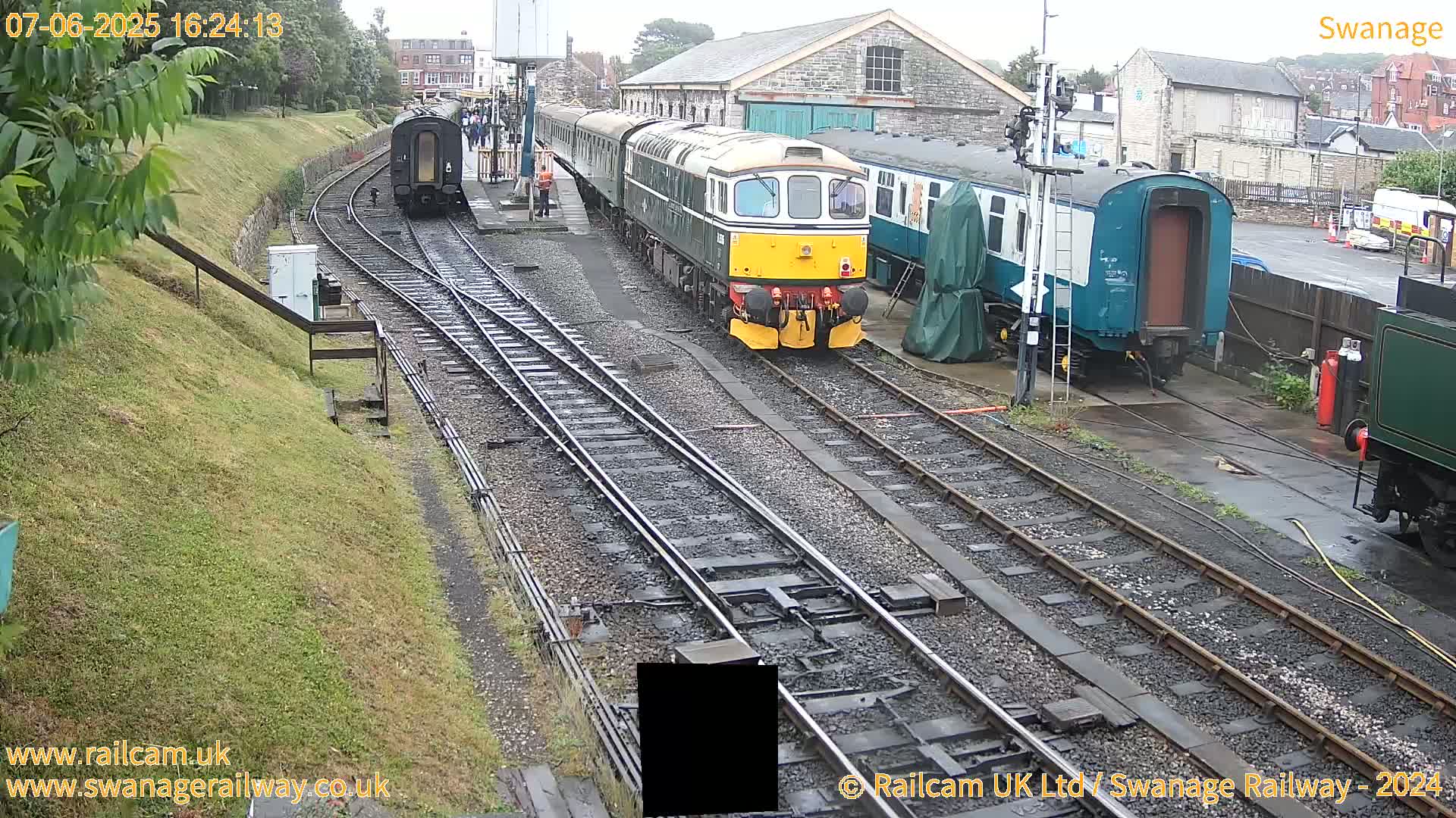 A train and several railway carriages are parked at a station on a cloudy day.