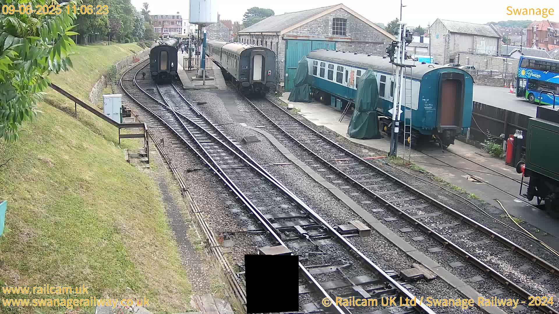 Several railway carriages are parked along multiple train tracks on an overcast day, with a bus visible in the background.