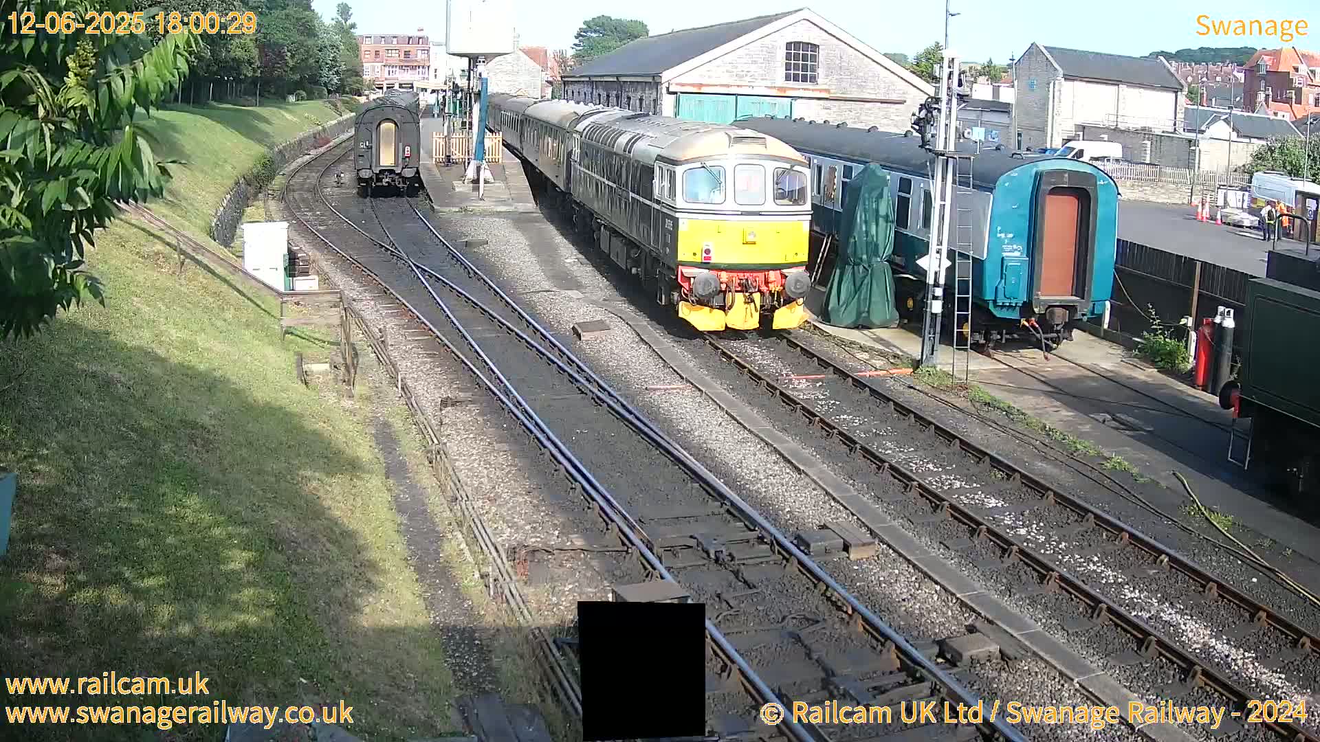 A sunny day at a train station shows multiple train cars and locomotives on several tracks, some parked and others moving.