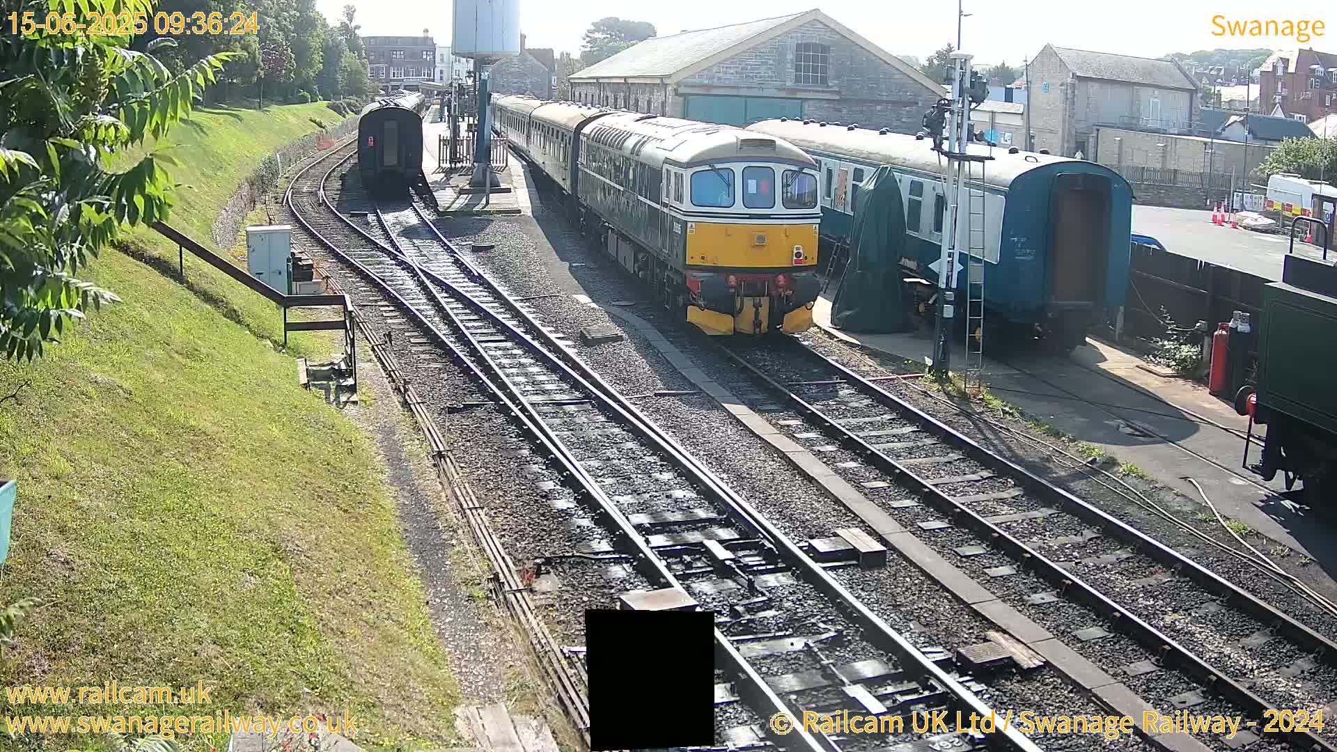 A diesel locomotive leads a train of passenger cars along railway tracks on a sunny day.