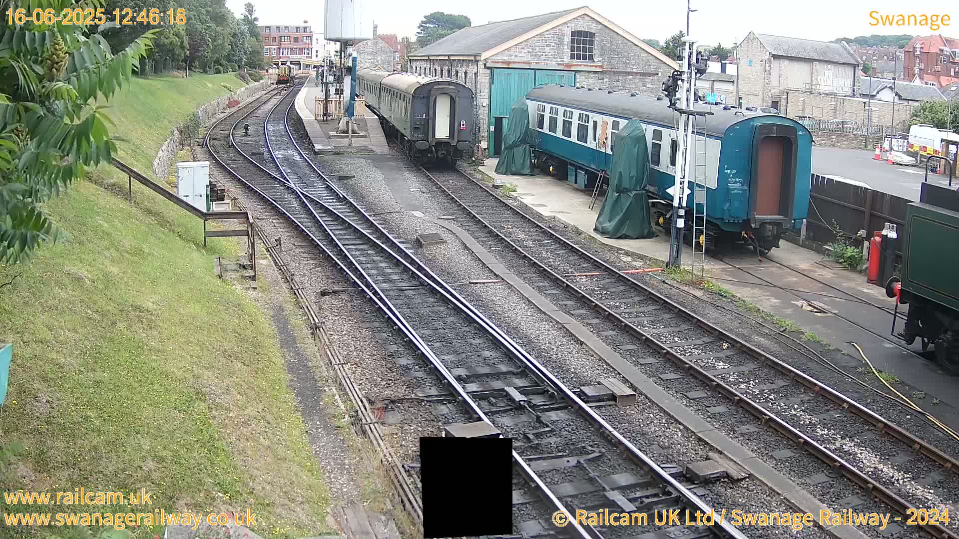 Several railway cars are parked on multiple train tracks beside a railway station building on an overcast day.