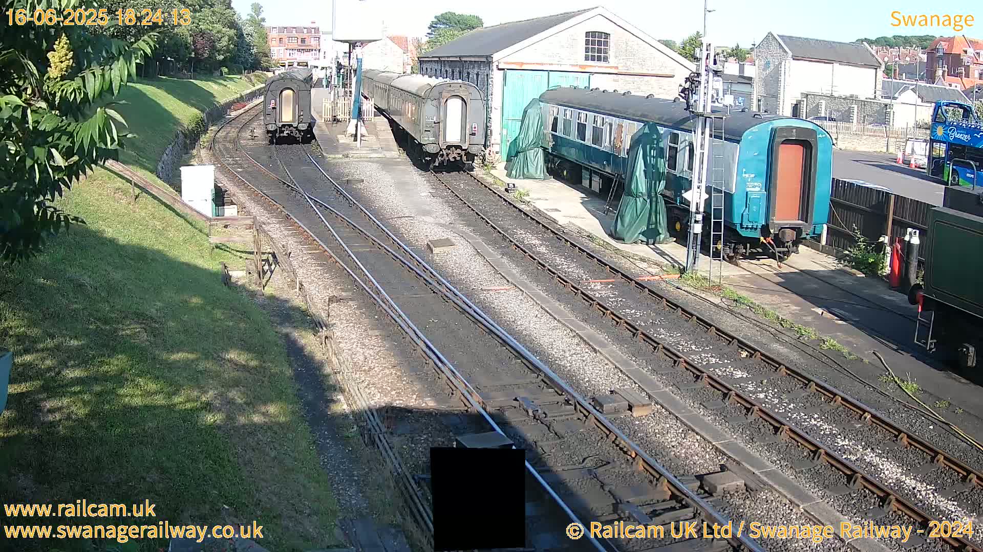 Several railway carriages are parked on train tracks outside a stone building on a sunny day.