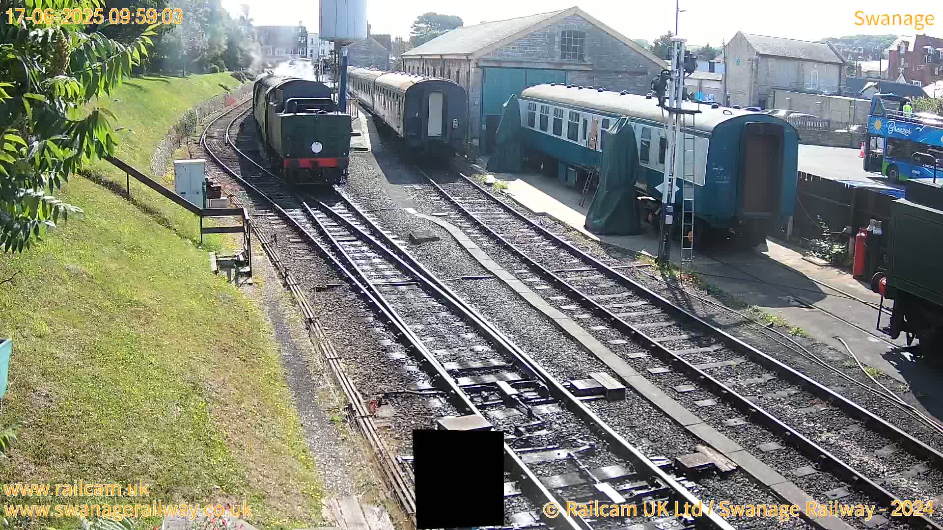 A steam train is pulling passenger cars along railway tracks on a sunny day.