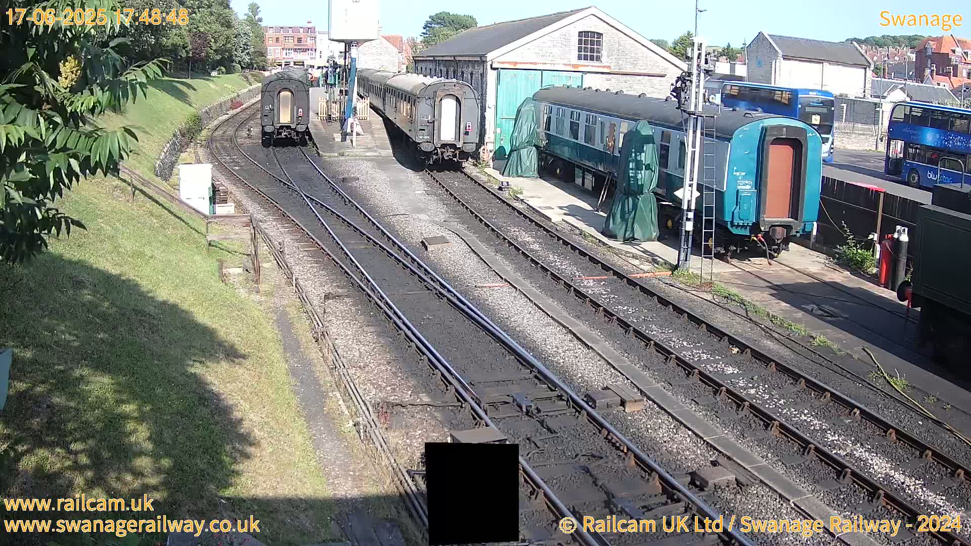 Several railway carriages are parked on train tracks next to a railway station building on a sunny day.