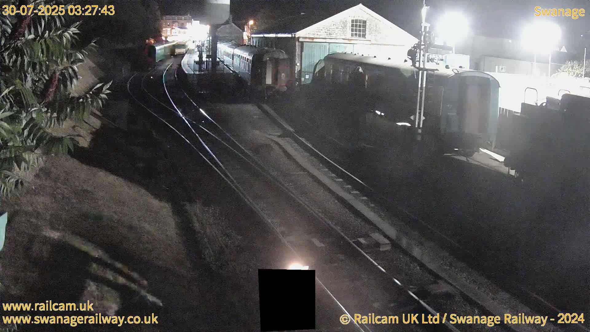 Multiple railway carriages and locomotives are parked on sunny railway tracks at a station.