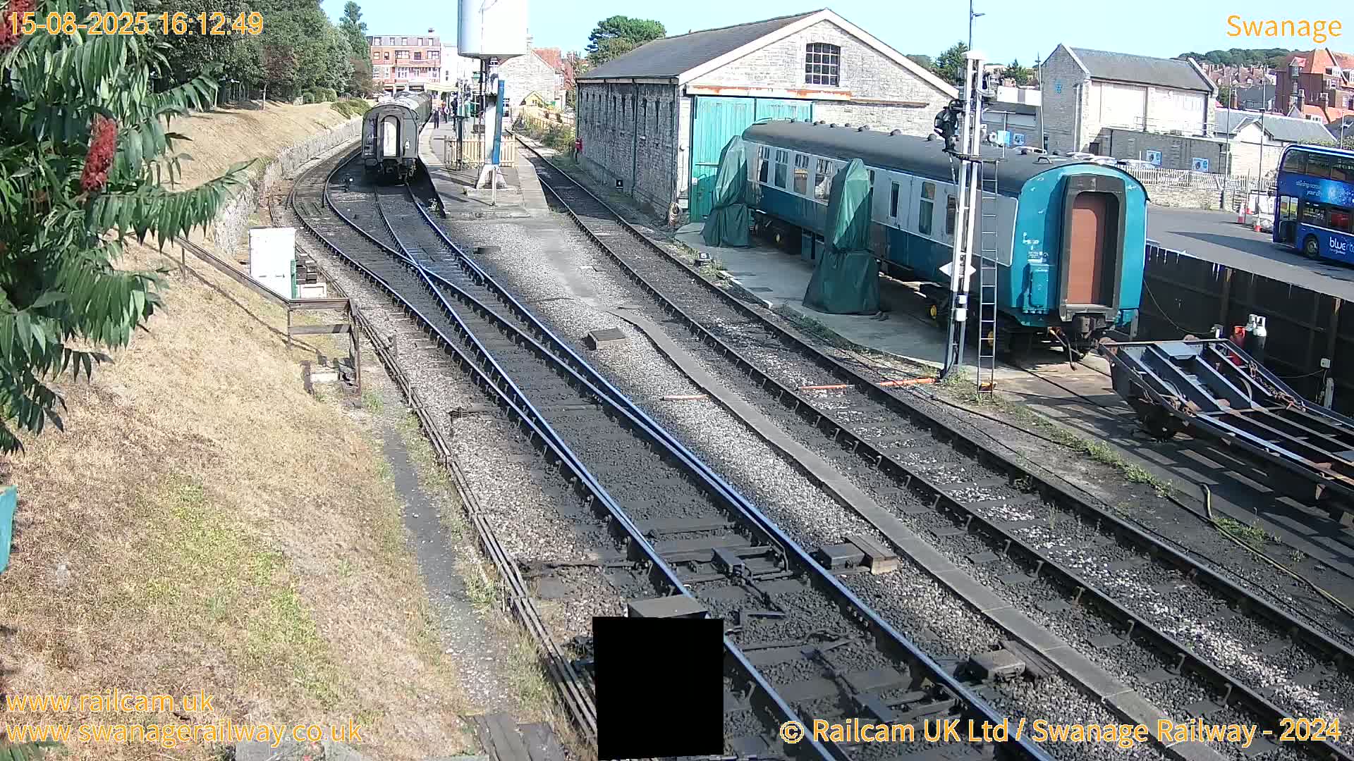 Multiple railway carriages and locomotives are parked on sunny railway tracks at a station.