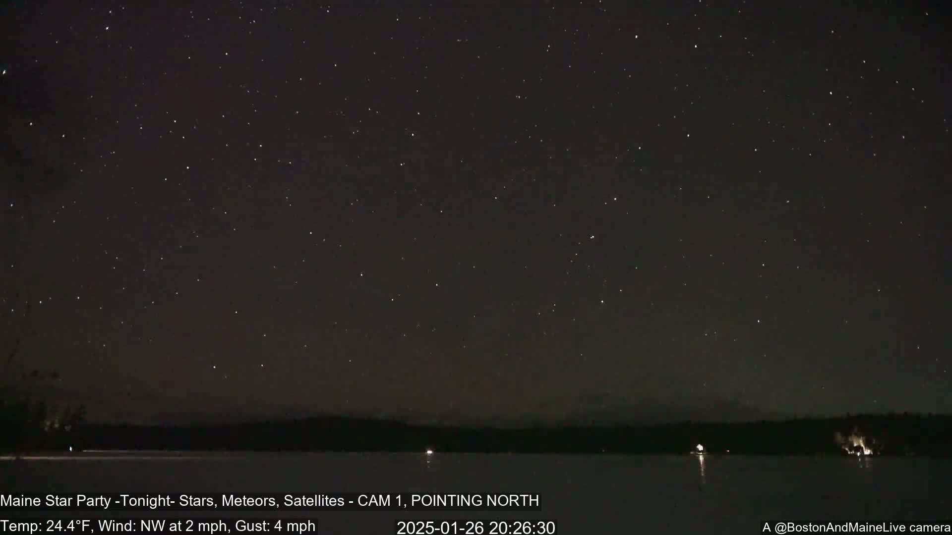 A nighttime long exposure shows a dark sky full of stars over a calm lake with a dark shoreline in a cold, windy location.