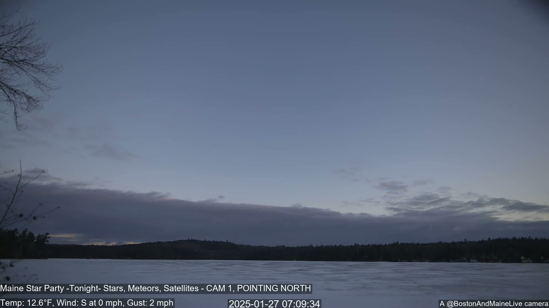 A frozen lake is visible beneath a mostly clear, twilight sky with a low layer of clouds, under calm, cold conditions.