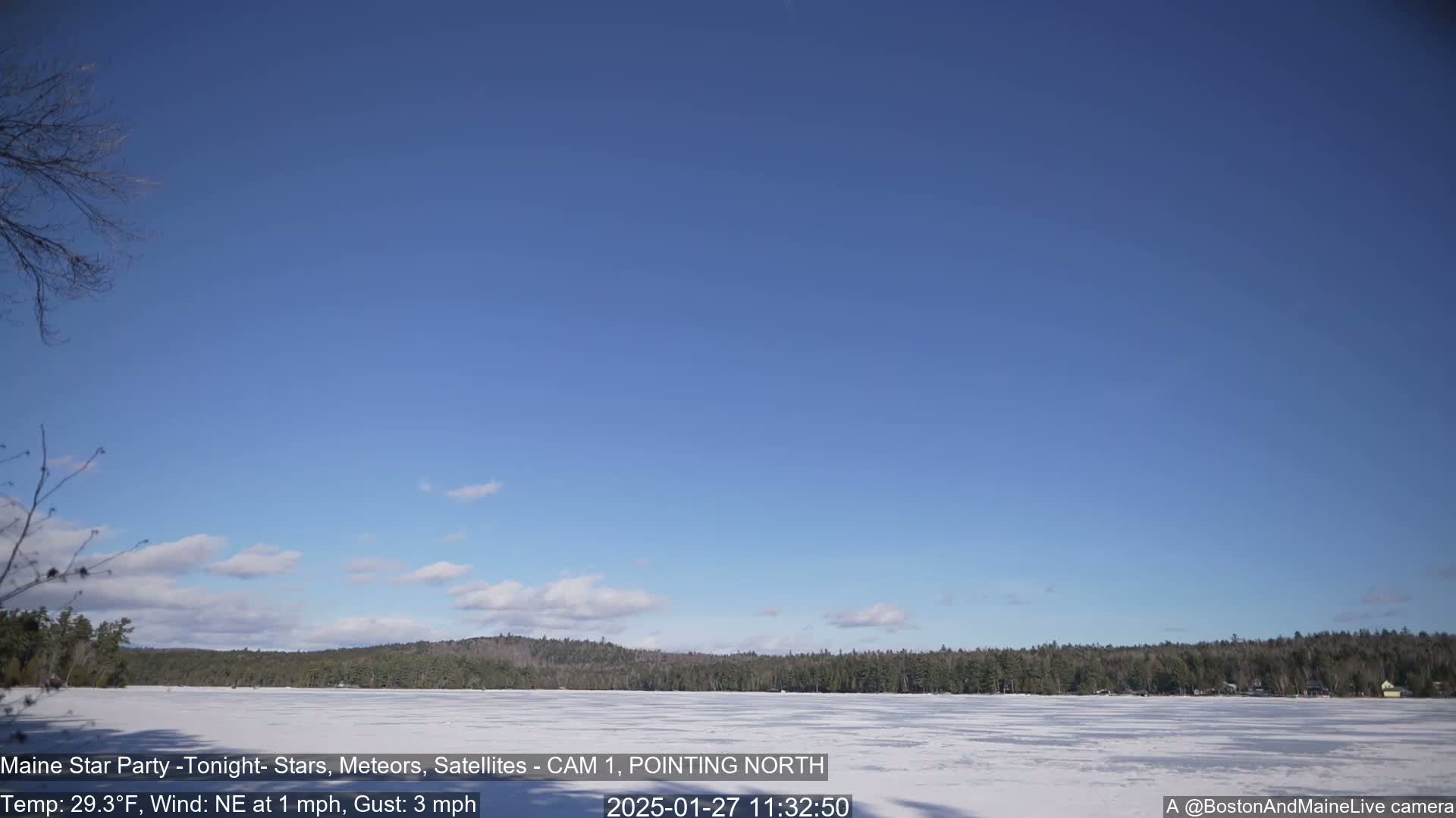 A mostly clear blue sky over a frozen lake with a snow-covered shoreline and dark evergreen trees beyond.