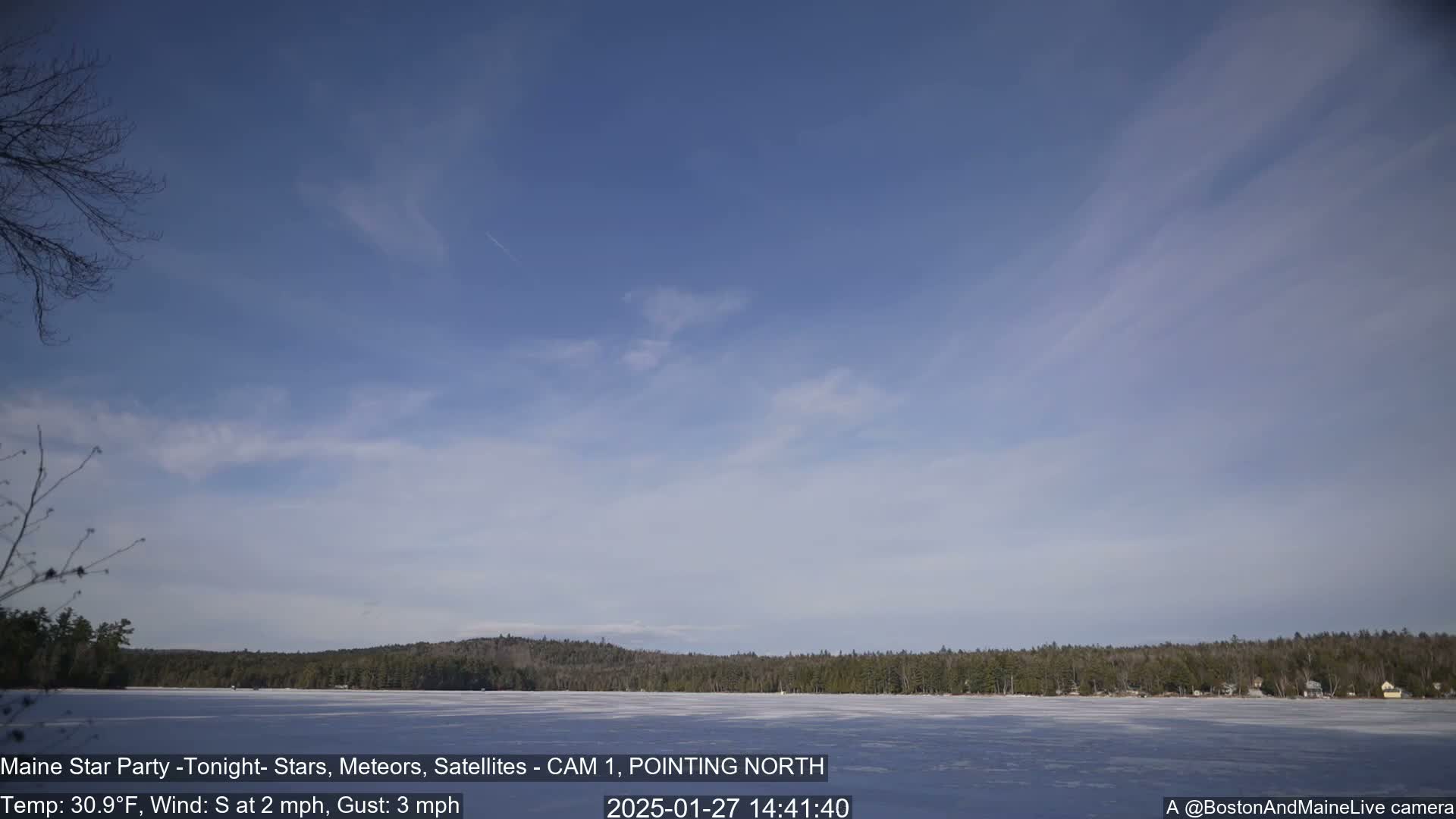 A frozen lake stretches before a treeline under a mostly clear, light blue sky.
