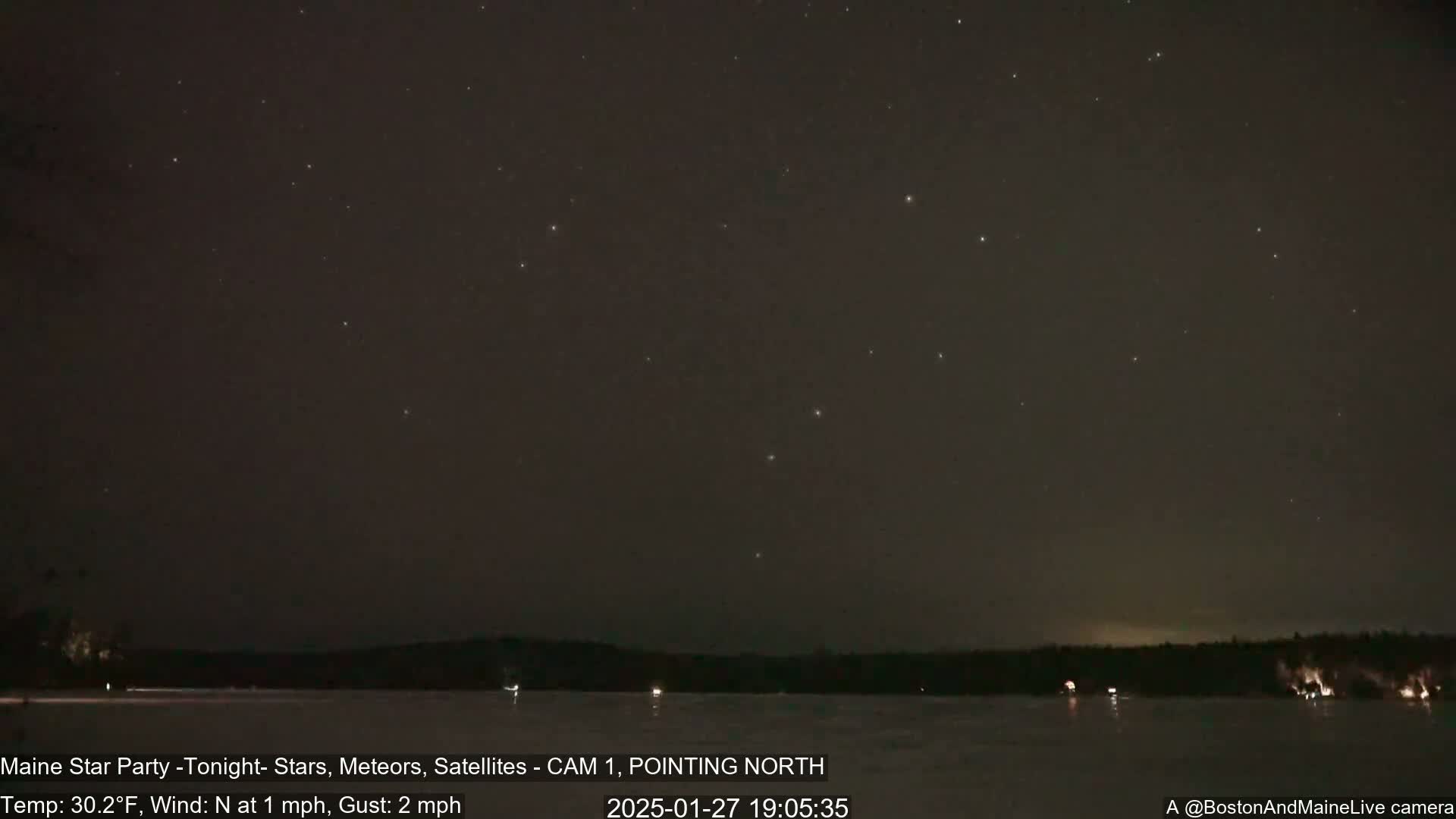 A night sky filled with stars is visible over a frozen lake and dark treeline, under a clear, cold night with a north wind of 1 mph and gusts up to 2 mph.
