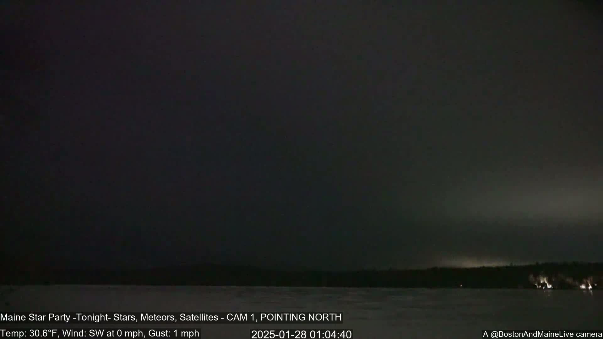A dark, nighttime scene shows a body of water with a tree line on the far side under a mostly clear, dark sky.