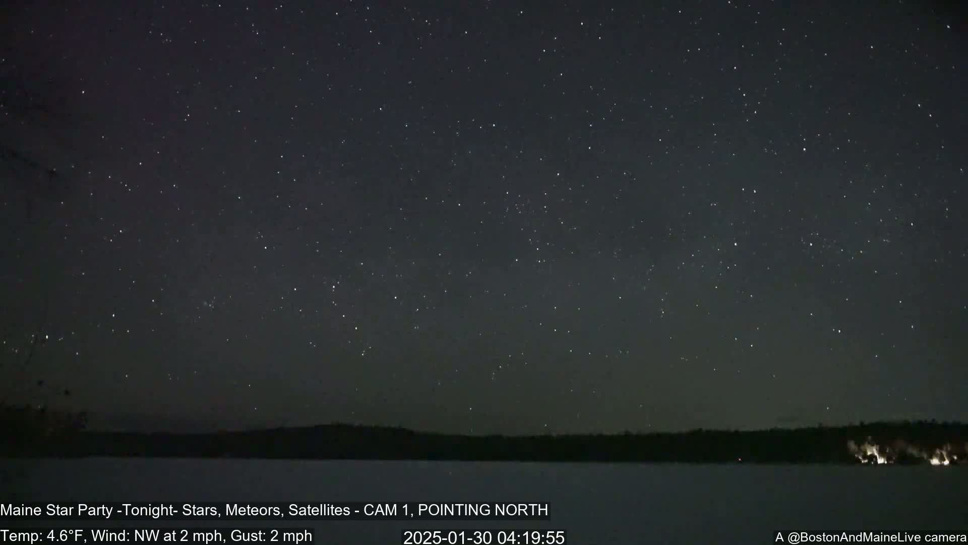 A nighttime, star-filled sky over a snow-covered lake and dark treeline, with a northwest wind blowing at 2 mph and gusts of 2 mph.