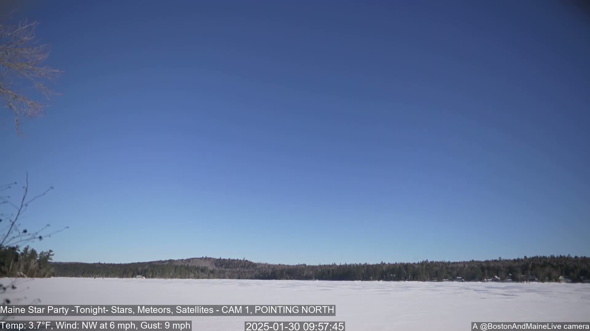 A frozen lake stretches out beneath a clear blue sky, with a dark line of trees visible on the far shore.