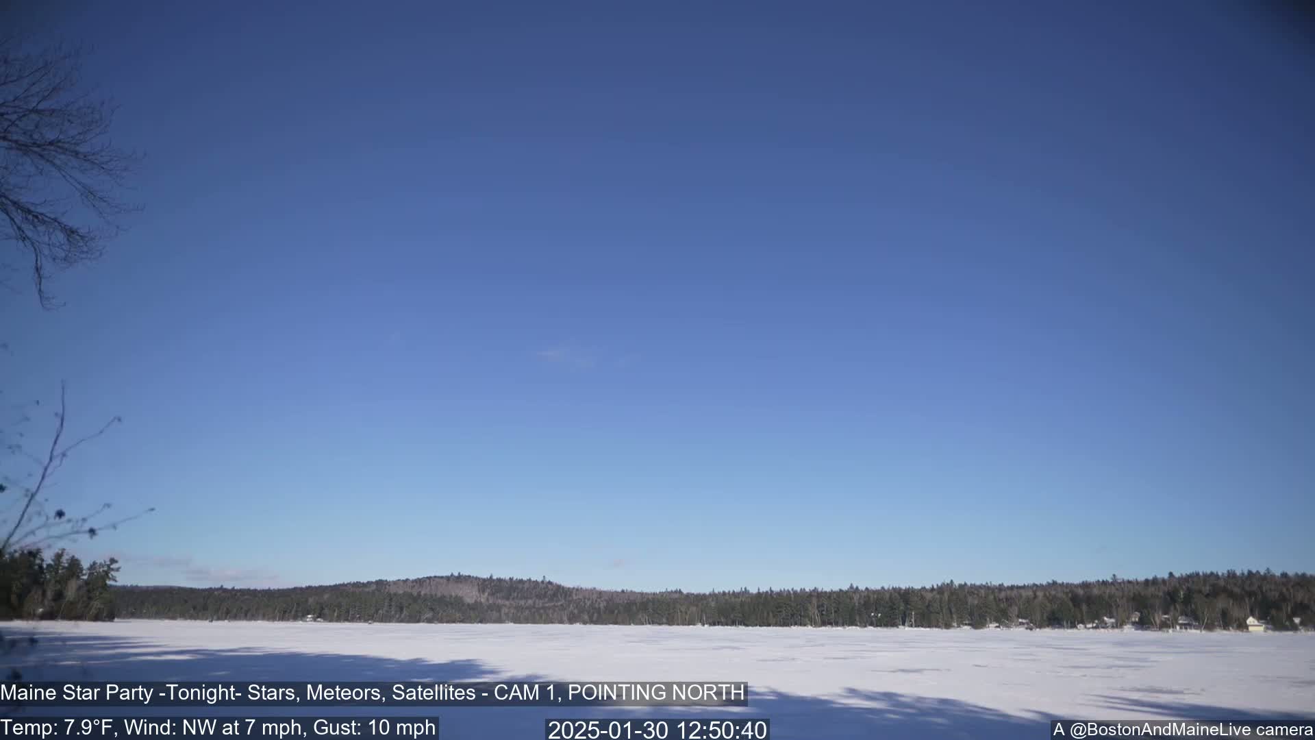 A frozen lake is visible, bordered by a snow-covered shoreline and a dark forest under a clear blue sky.