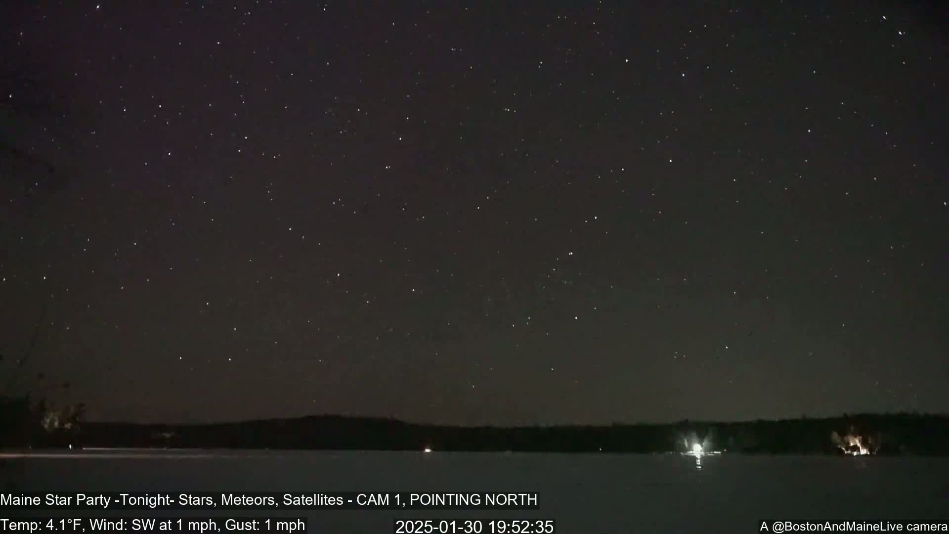 A dark, star-filled night sky over a frozen lake, with a slight southwest wind.