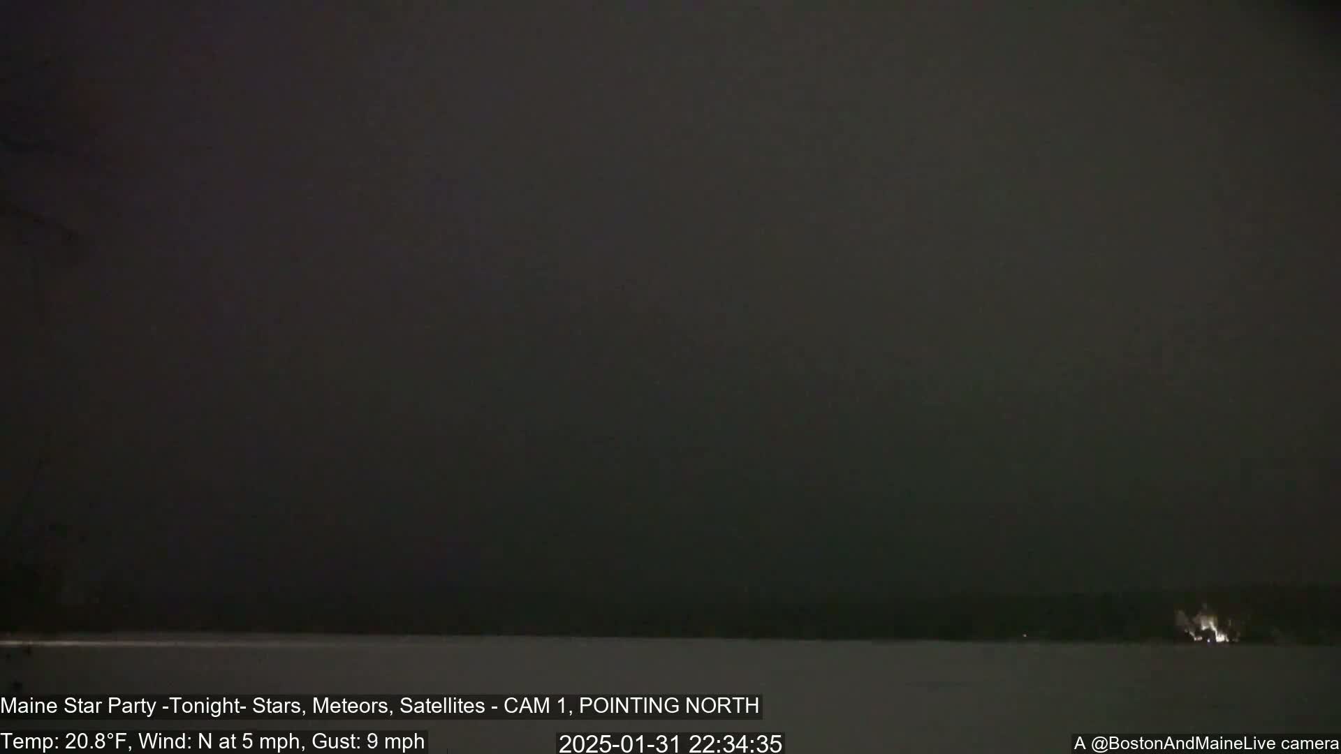 A dark, nighttime scene shows a mostly featureless, hazy sky over a snow-covered ground with a faint light source in the distance under a 20.8°F temperature with a 5 mph northerly wind and 9 mph gusts.