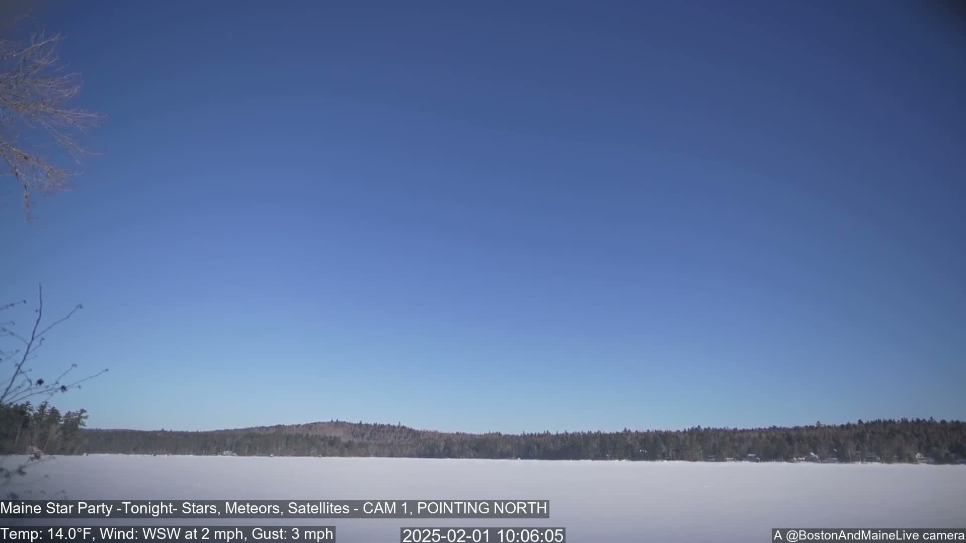 A snow-covered frozen lake is visible under a clear blue sky with a slight wind.