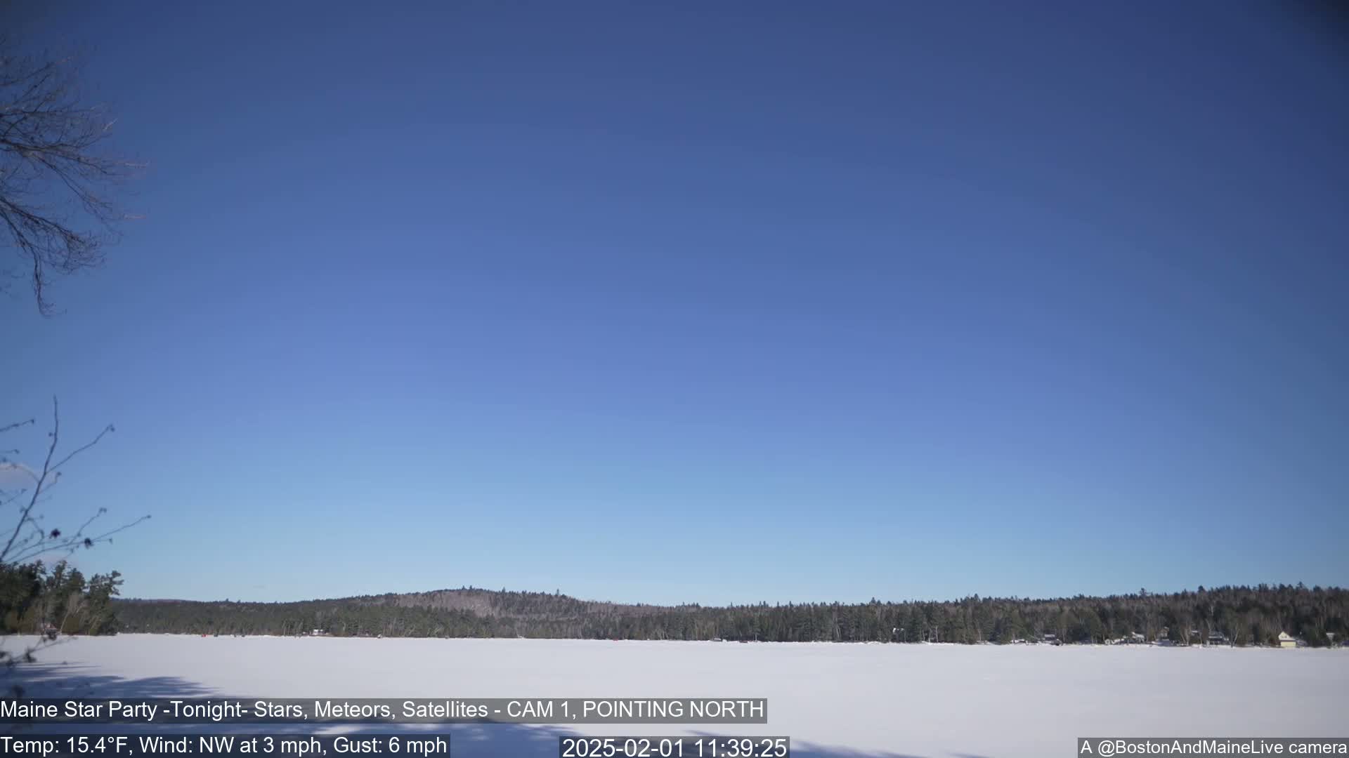 A snow-covered lake is visible beneath a clear blue sky, with a dark treeline in the background under a cold, clear, and sunny sky.