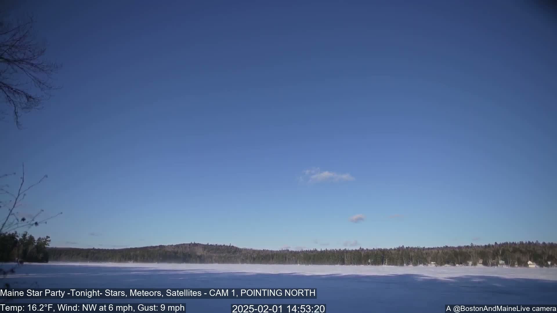A frozen lake is visible under a mostly clear blue sky, with a thin line of dark trees and buildings on the far shore.