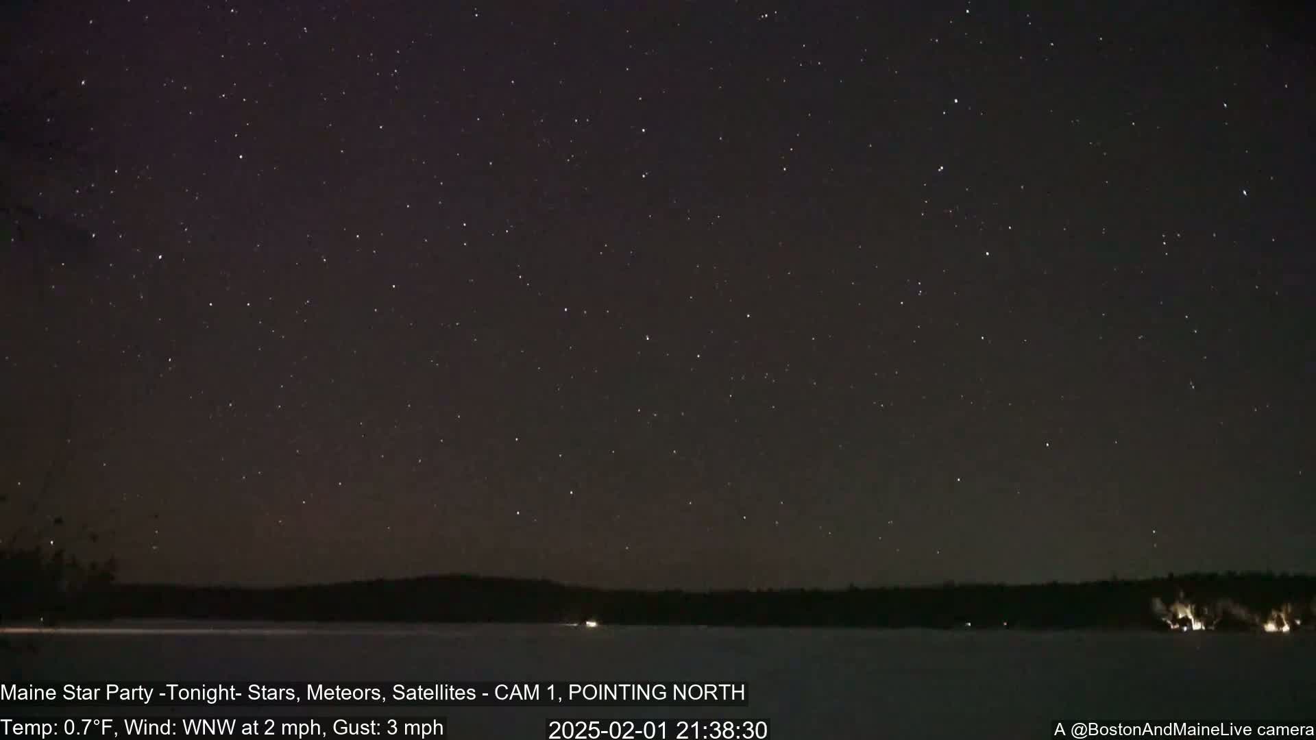 A nighttime long shot shows a clear, star-filled sky over a dark, frozen lake and distant trees under a wind of 2 mph with gusts up to 3 mph and a temperature of 0.7°F.