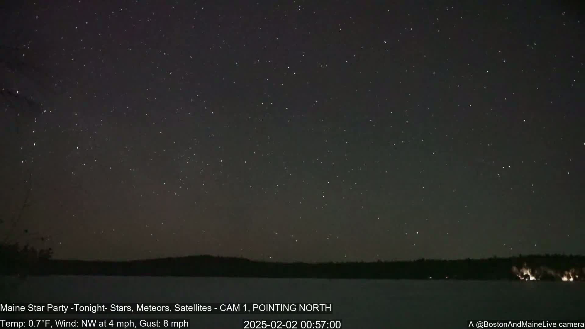 A nighttime view of a star-filled sky over a dark, snow-covered landscape with a slight northwest wind.