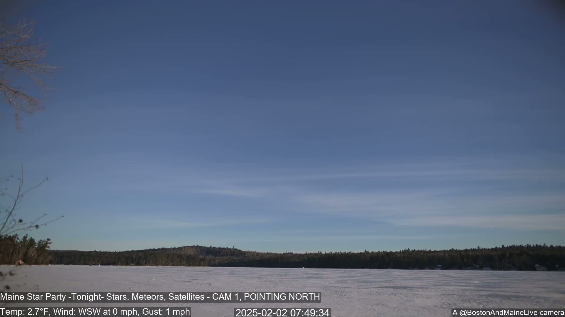 A frozen lake is visible beneath a clear, light-blue sky, with a dark treeline in the background.
