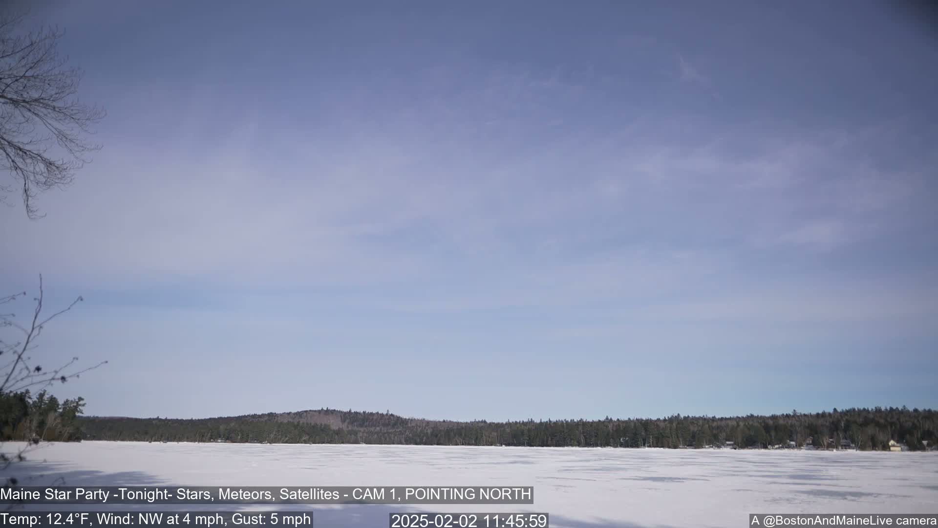A frozen lake is visible, bordered by a treeline under a mostly clear, light blue sky.