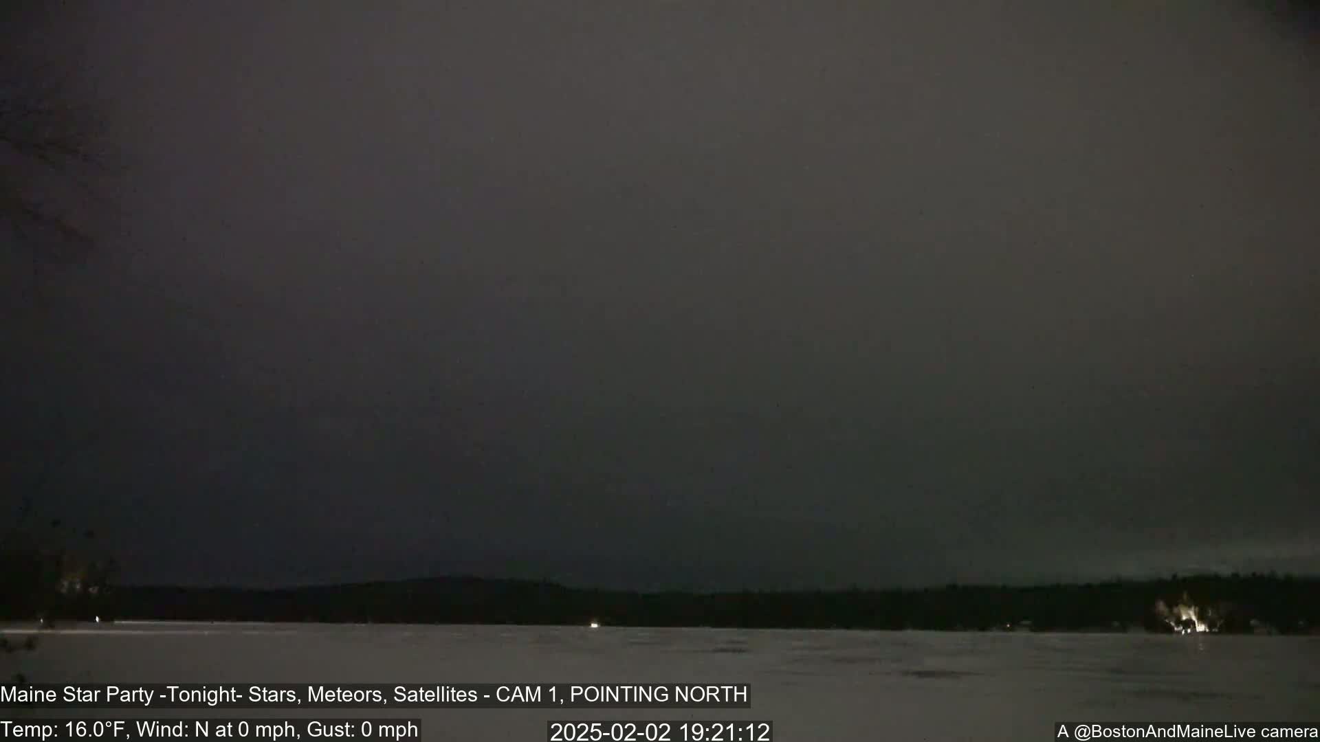 A dark, calm night scene shows a body of water with a dark shoreline under an overcast sky.
