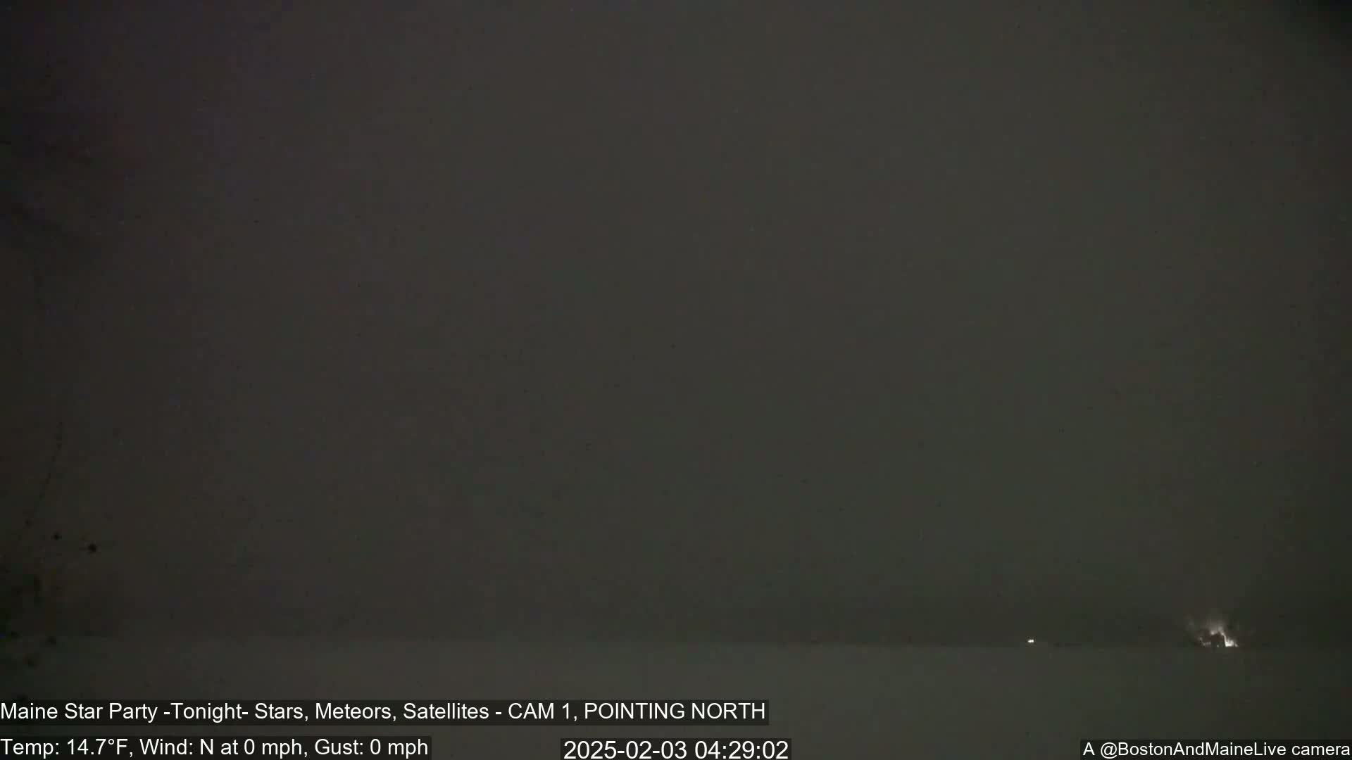 A dark, nighttime scene shows a mostly clear sky with a few faint lights visible on the horizon under calm, cold conditions.