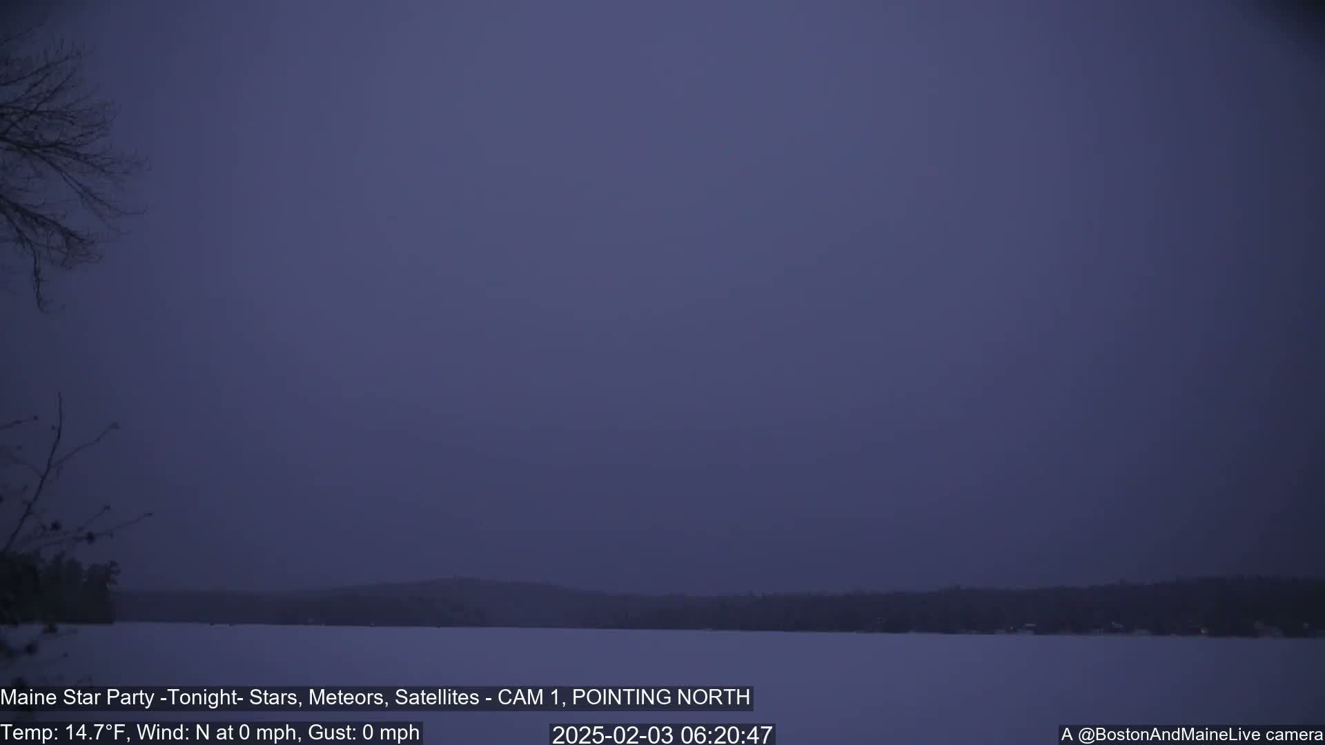 A calm, dark blue pre-dawn sky overlooks a snow-covered lake and distant trees.