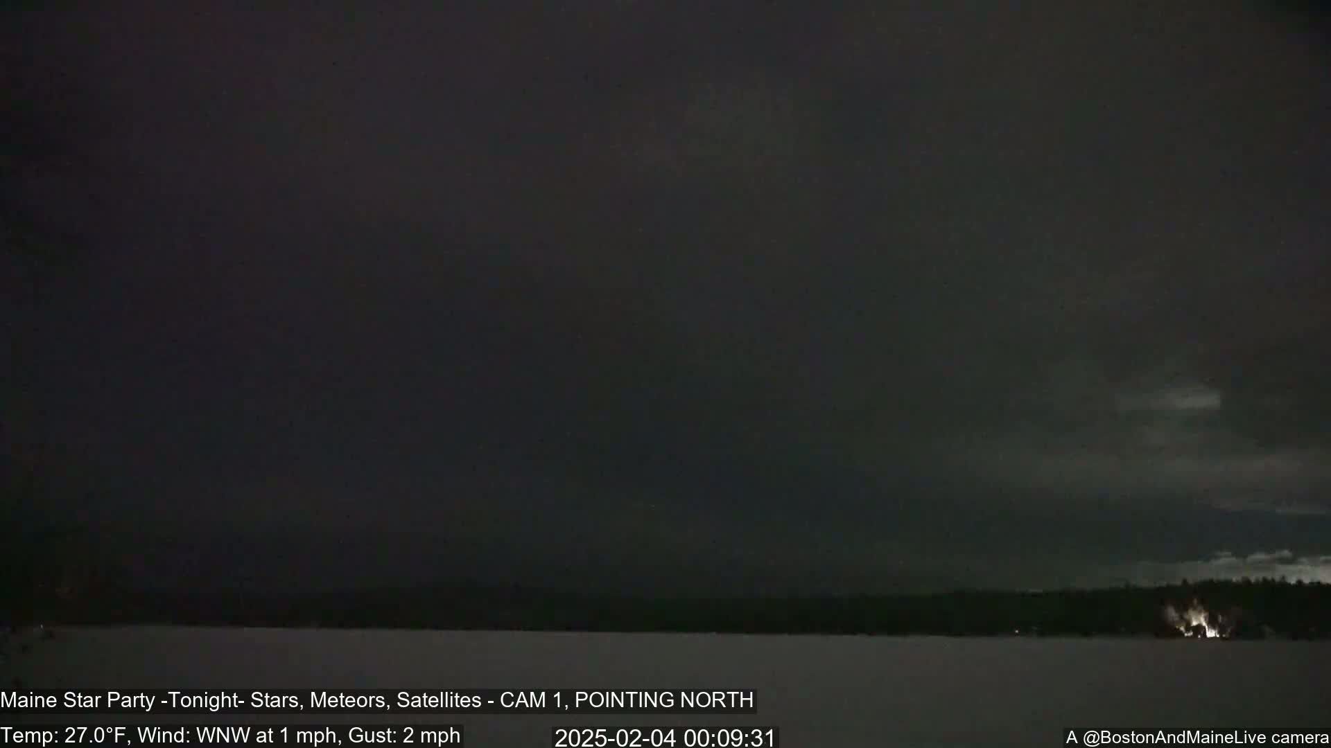 A dark, nighttime scene shows a mostly clear sky over a snow-covered landscape with a line of trees and faint lights in the distance, under a 27°F temperature with a 1 mph wind.