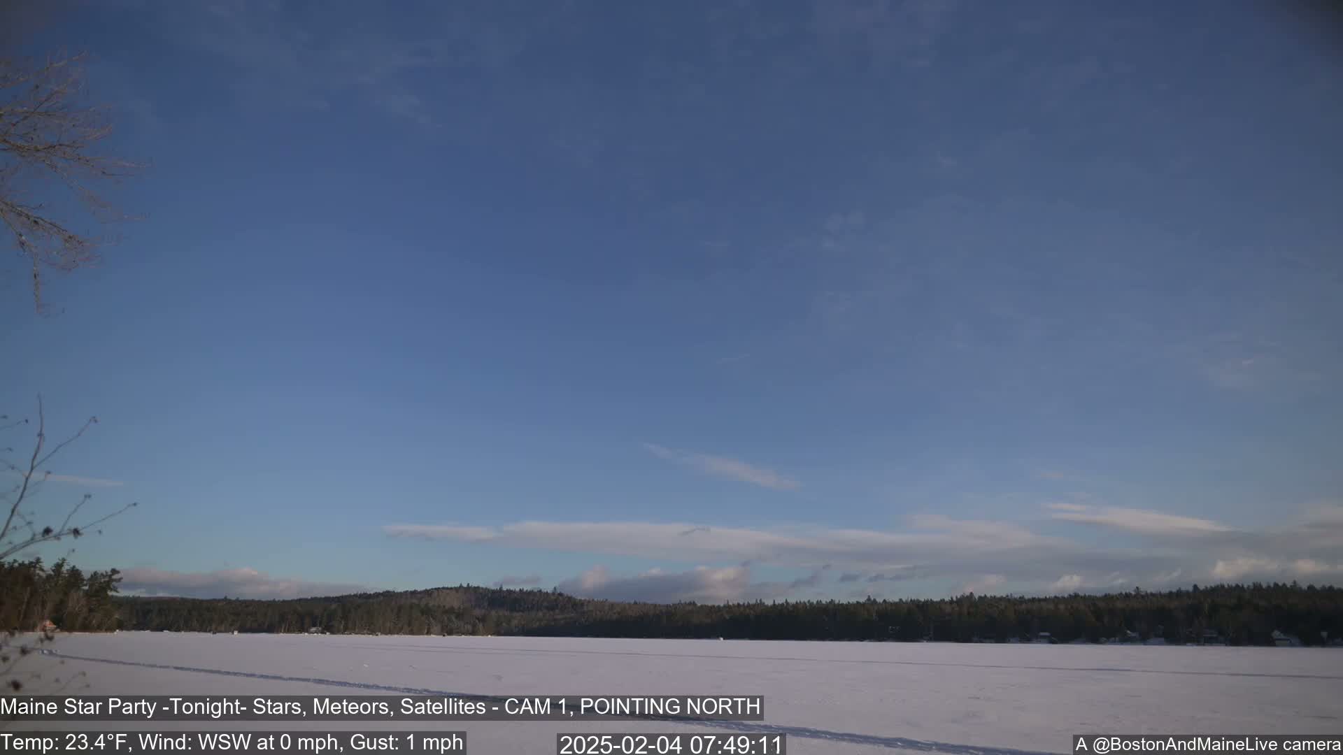 A frozen lake is visible beneath a mostly clear, light blue sky with a few thin clouds, and a treeline stretches across the horizon.