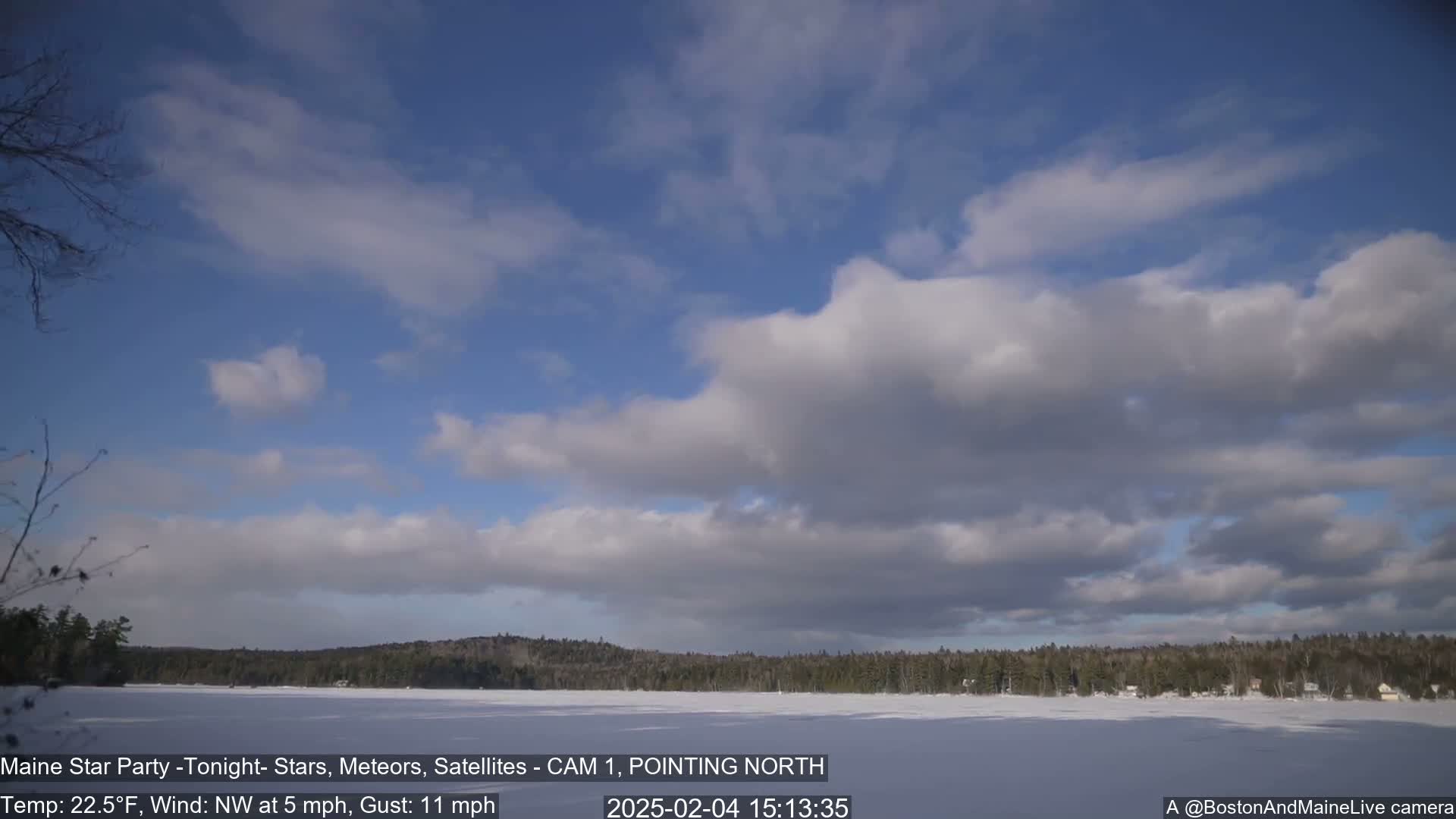 A partly cloudy blue sky over a snow-covered frozen lake with a dark treeline in the background.