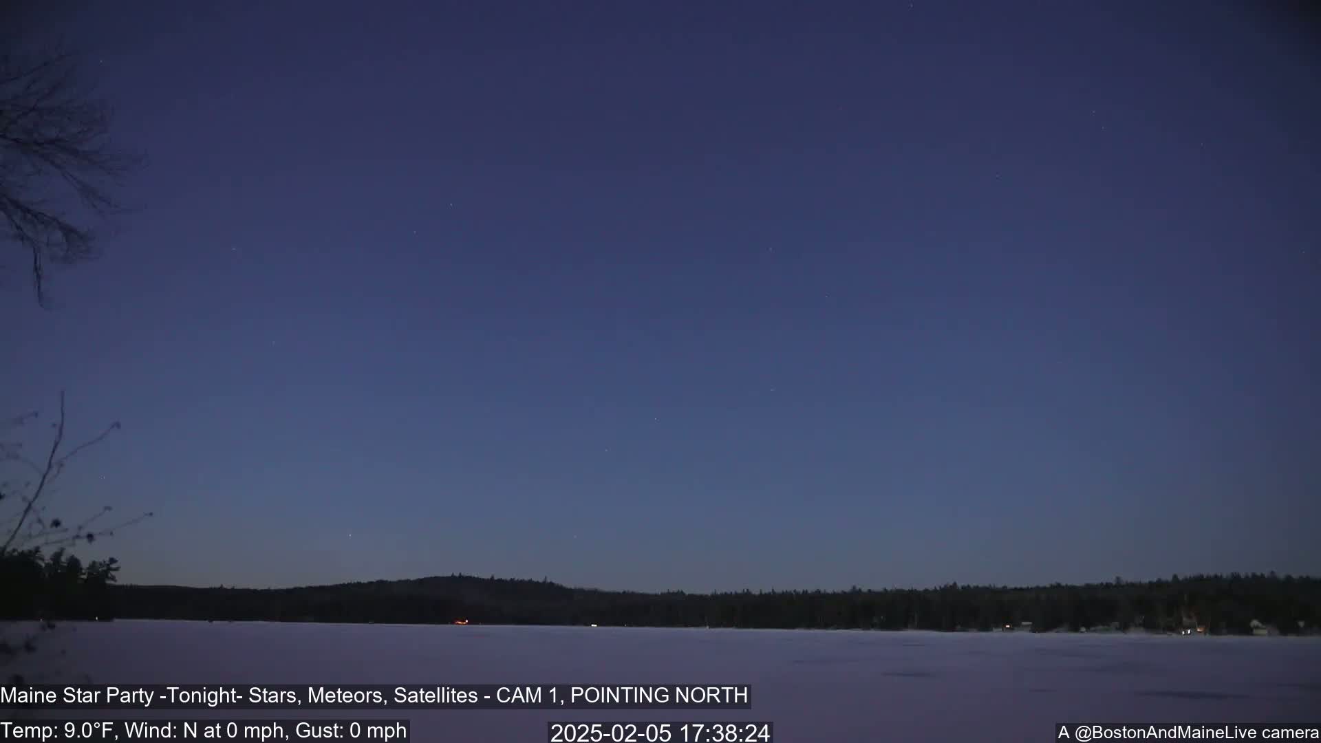 Under a clear, twilight sky, a frozen lake stretches out before a dark, snow-covered shoreline and a distant tree line.