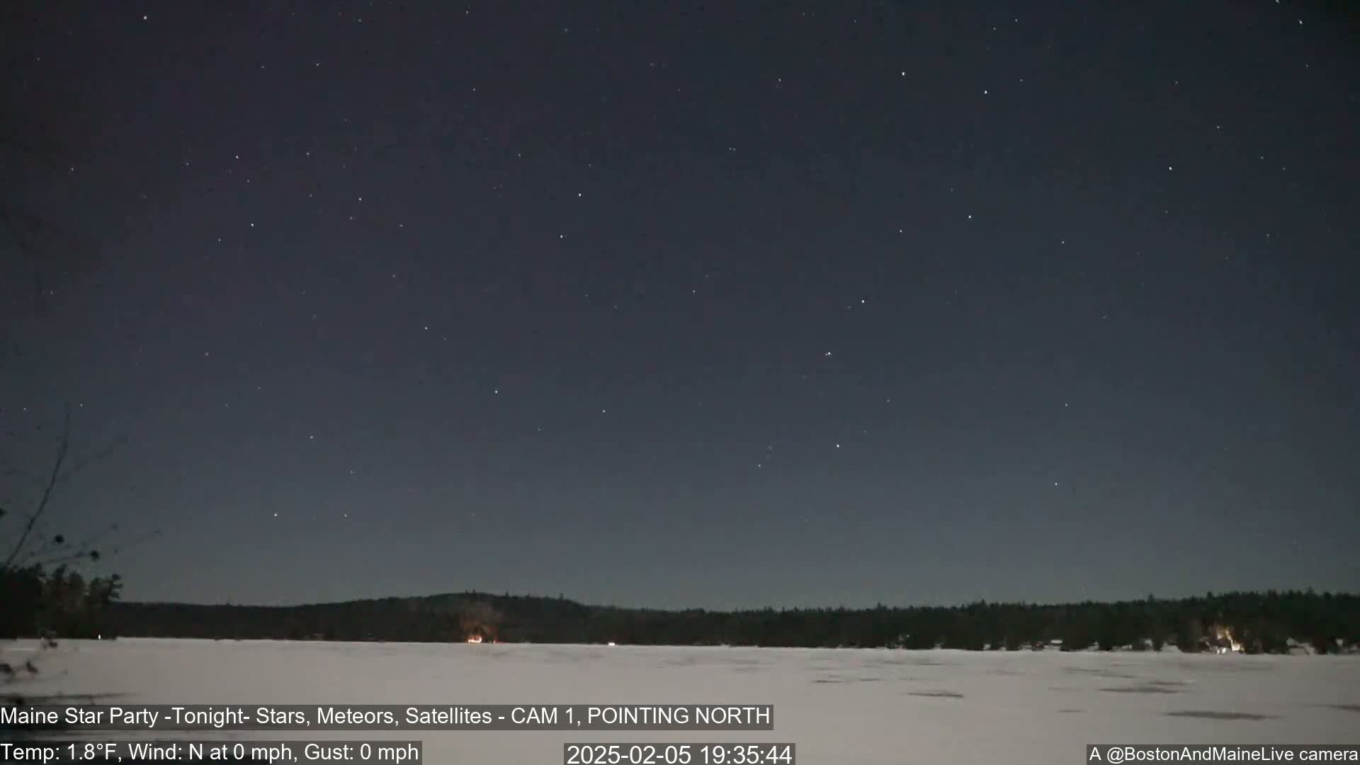 A clear, cold night sky filled with stars is visible over a snow-covered frozen lake and dark treeline.