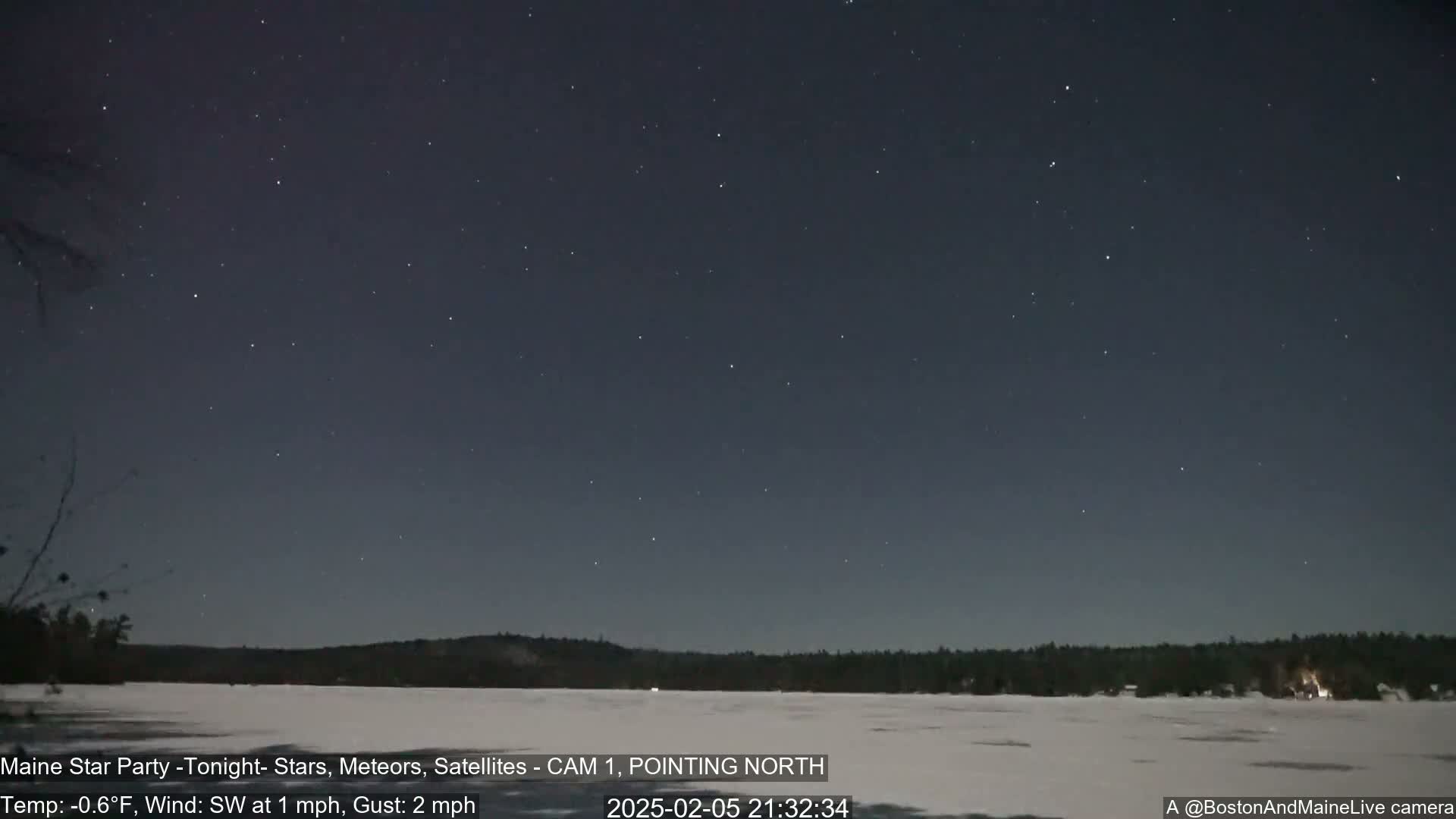 A starry night sky over a frozen lake and dark, snow-covered shoreline, with a light southwest wind at 1 mph and gusts up to 2 mph, and a temperature of -0.6°F.