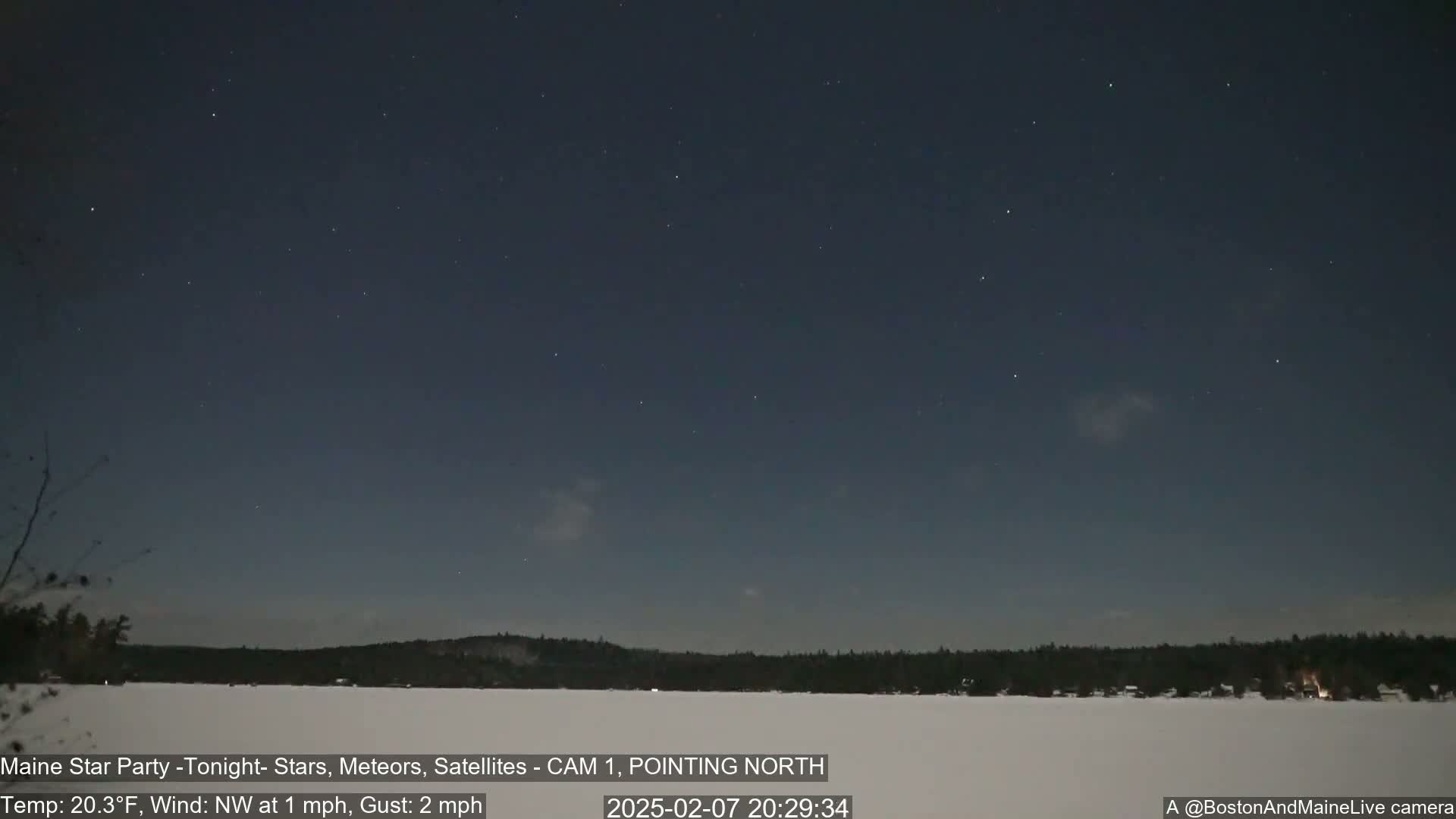 A mostly clear night sky with numerous stars over a snow-covered lake and dark tree line, with a northwest wind at 1 mph and gusts up to 2 mph.