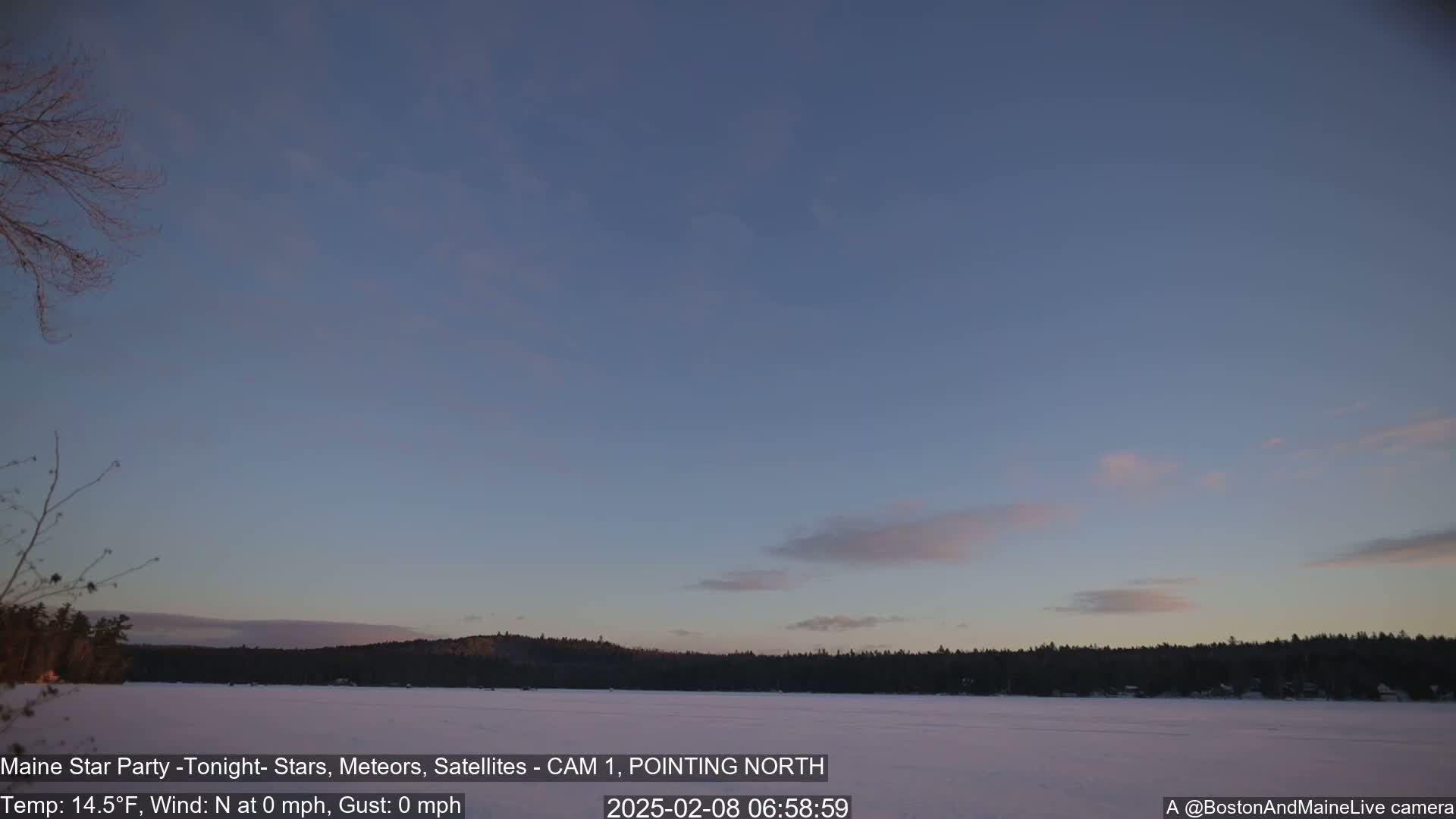 A calm, twilight scene shows a frozen lake reflecting a pale sky with a few wispy clouds, and a dark, tree-lined shore in the background.
