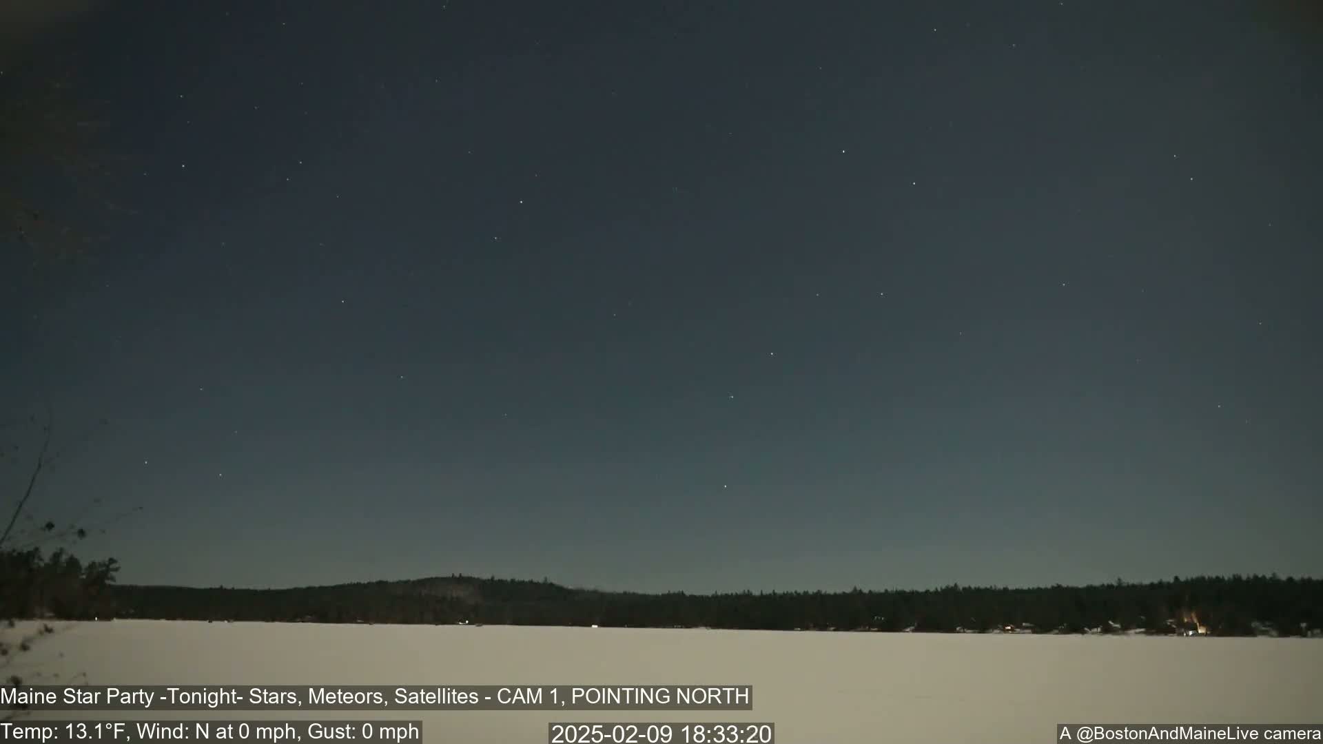 A calm, clear night sky with numerous stars visible over a snow-covered landscape and dark treeline.
