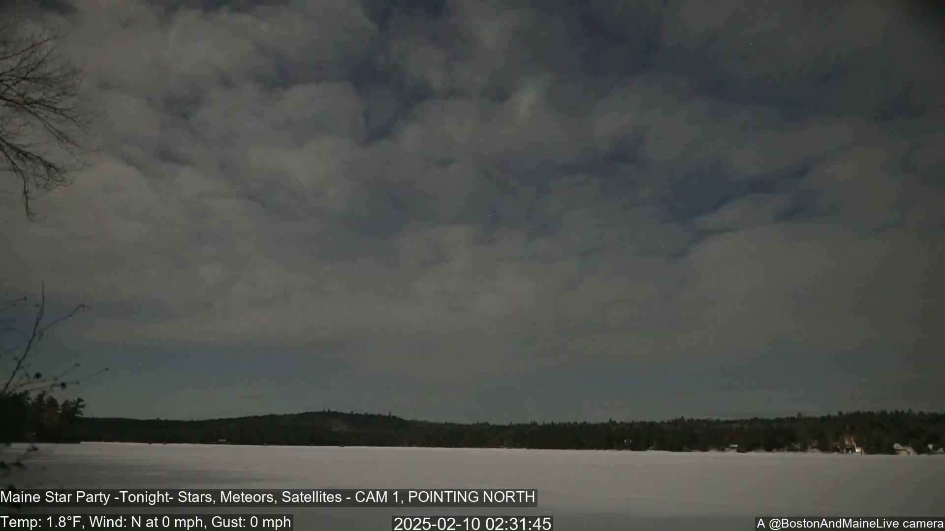 A frozen lake is visible under a mostly cloudy night sky with a calm wind.